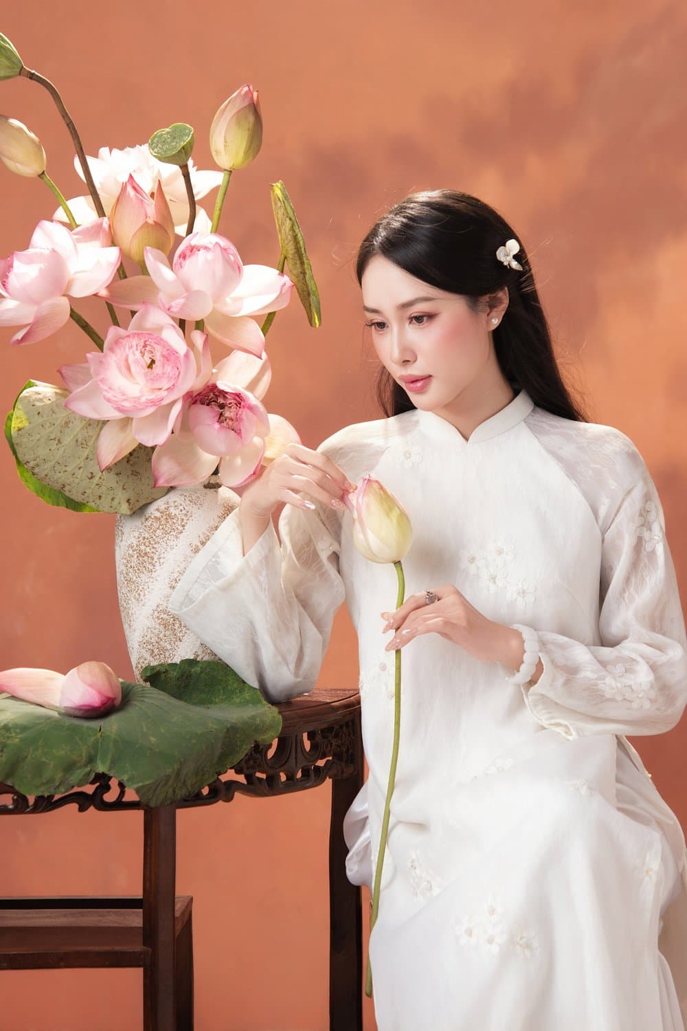 Thiếu nữ áo dài trắng cắm cành sen hồng, phông nâu đất — concept Sắc đất ấm trong studio