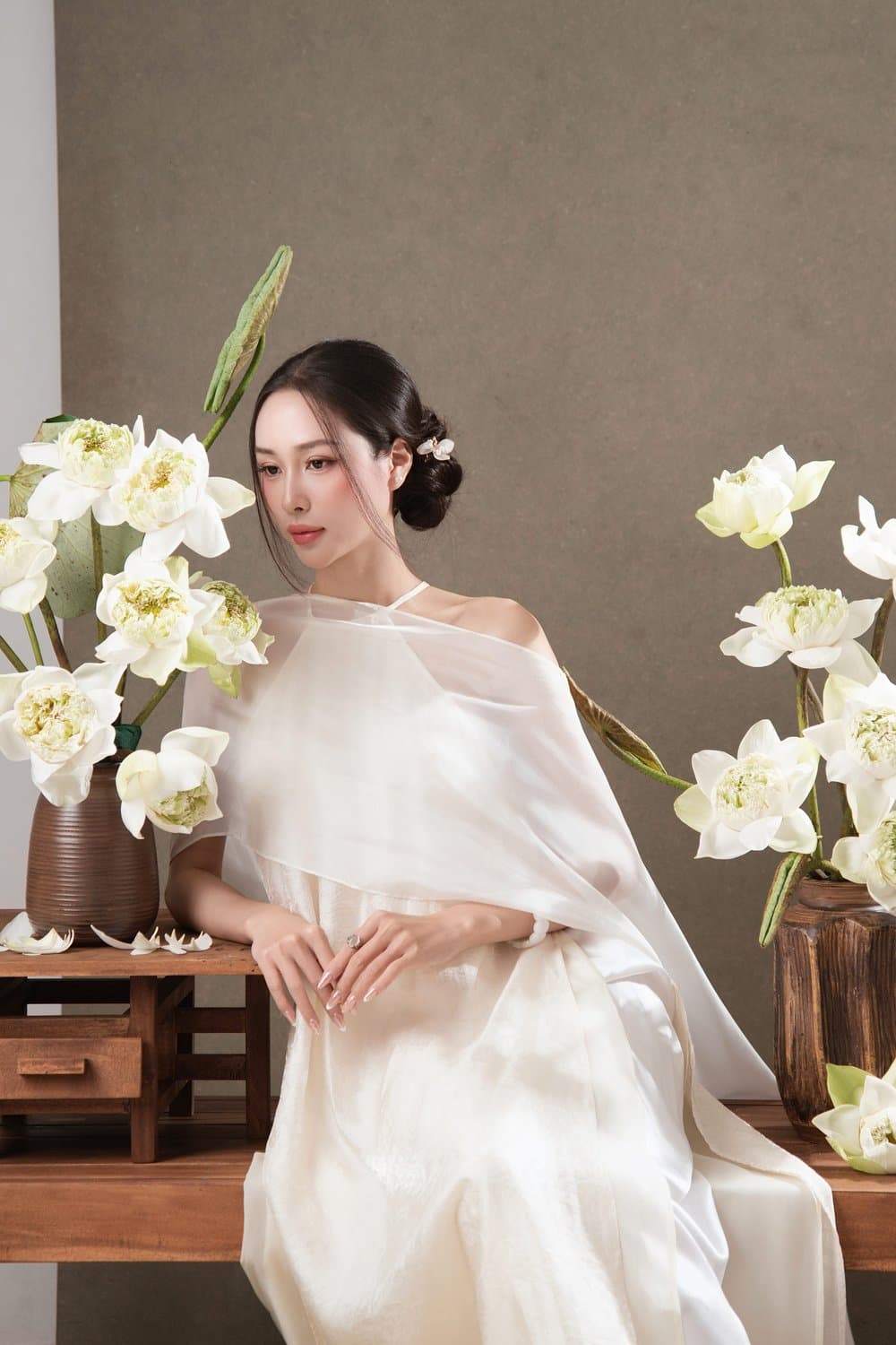 Ngồi bên bình sen trắng, voan trắng nhẹ, phông xám sáng — concept sen studio Trắng tinh khôi