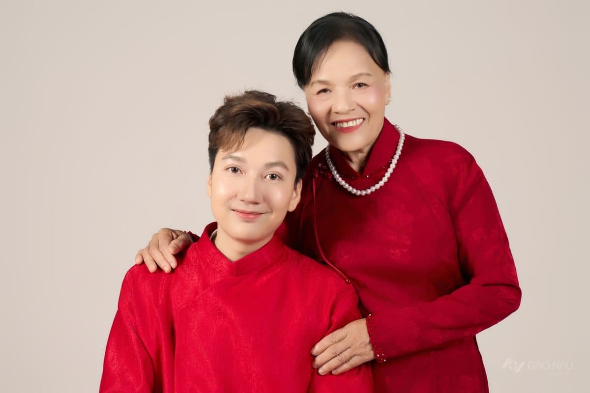 Hai mẹ con mặc áo đỏ đứng cạnh nhau trong studio, mẹ đặt tay lên vai con, cả hai cùng cười hiền