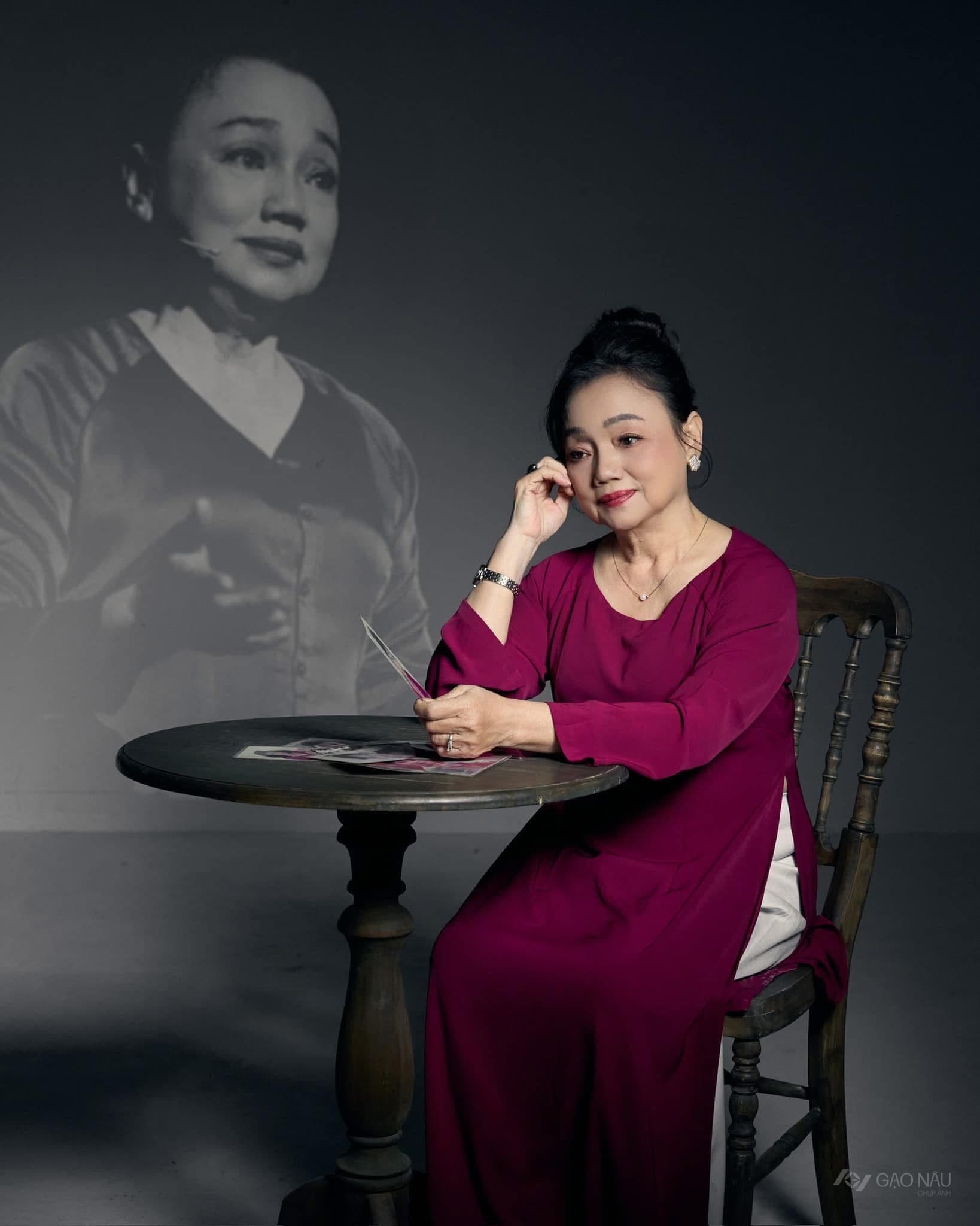 Nghệ sĩ Lý Kiều Hạnh ngồi tại studio Gạo Nâu, mặc áo đỏ, sau lưng là ảnh chân dung thời trẻ