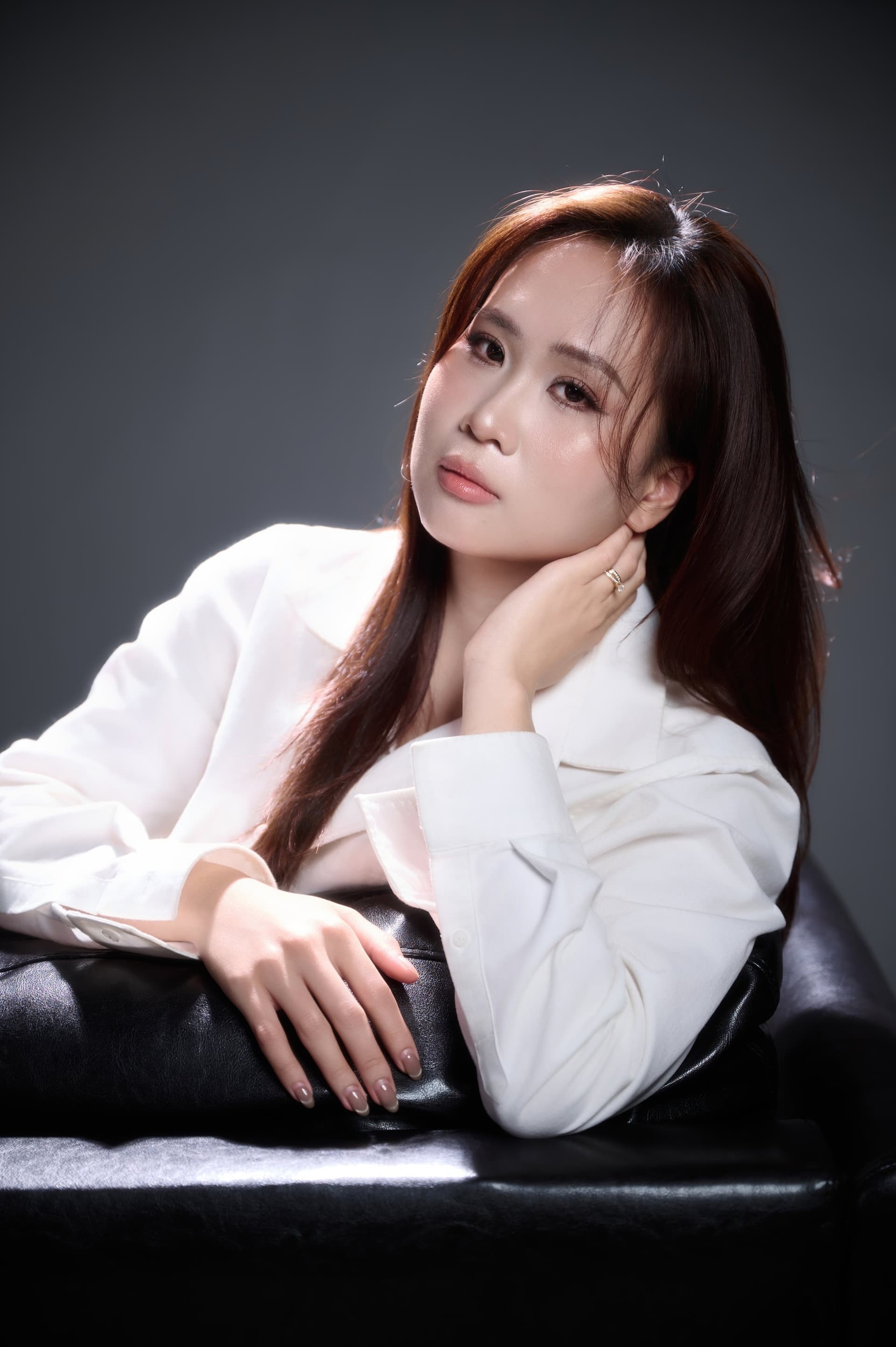 Người phụ nữ áo trắng ngồi xếp bằng thư thái, ánh mắt dịu — dáng quen của người đã có chỗ dựa lâu năm