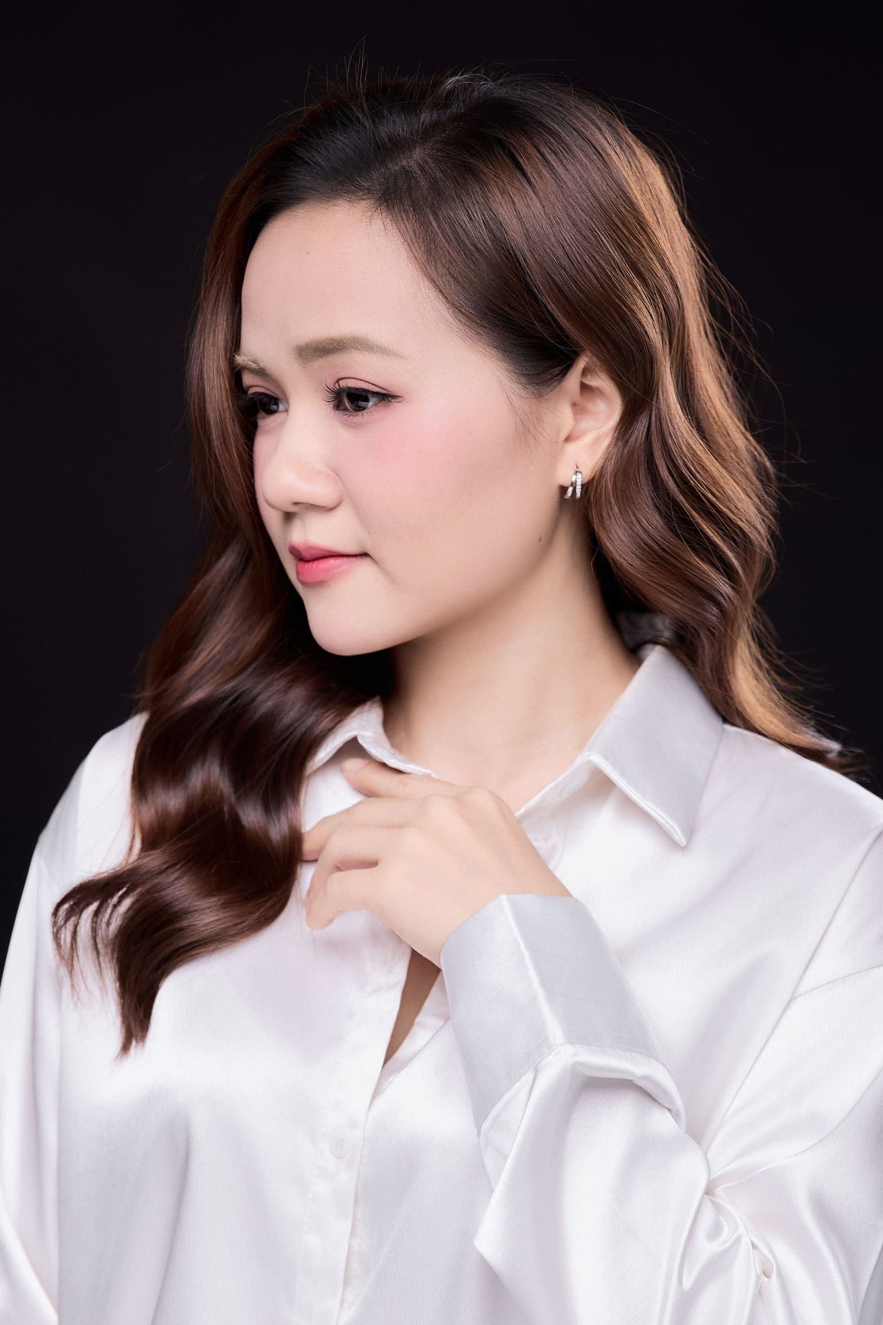 Thu Thảo mặc áo sơ mi trắng, dáng đứng nhẹ một bên, gương mặt trầm tĩnh — một người đã quen để dành những điều của mình lại sau