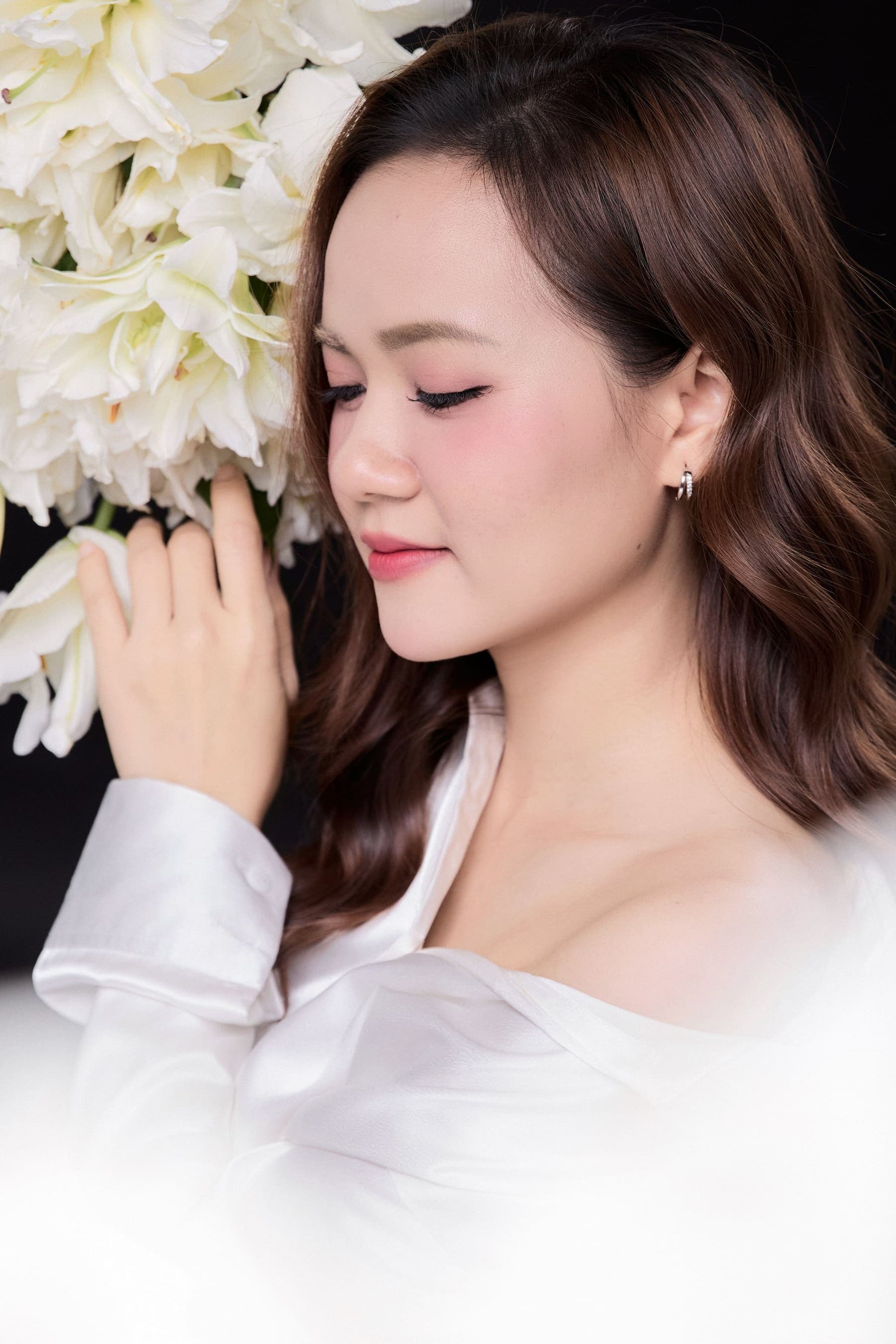 Thu Thảo nhắm mắt ôm bó hoa lily trắng, dáng người dịu — một cuộc hẹn đầu với tháng Tám đã được giữ lại từ tháng Tư