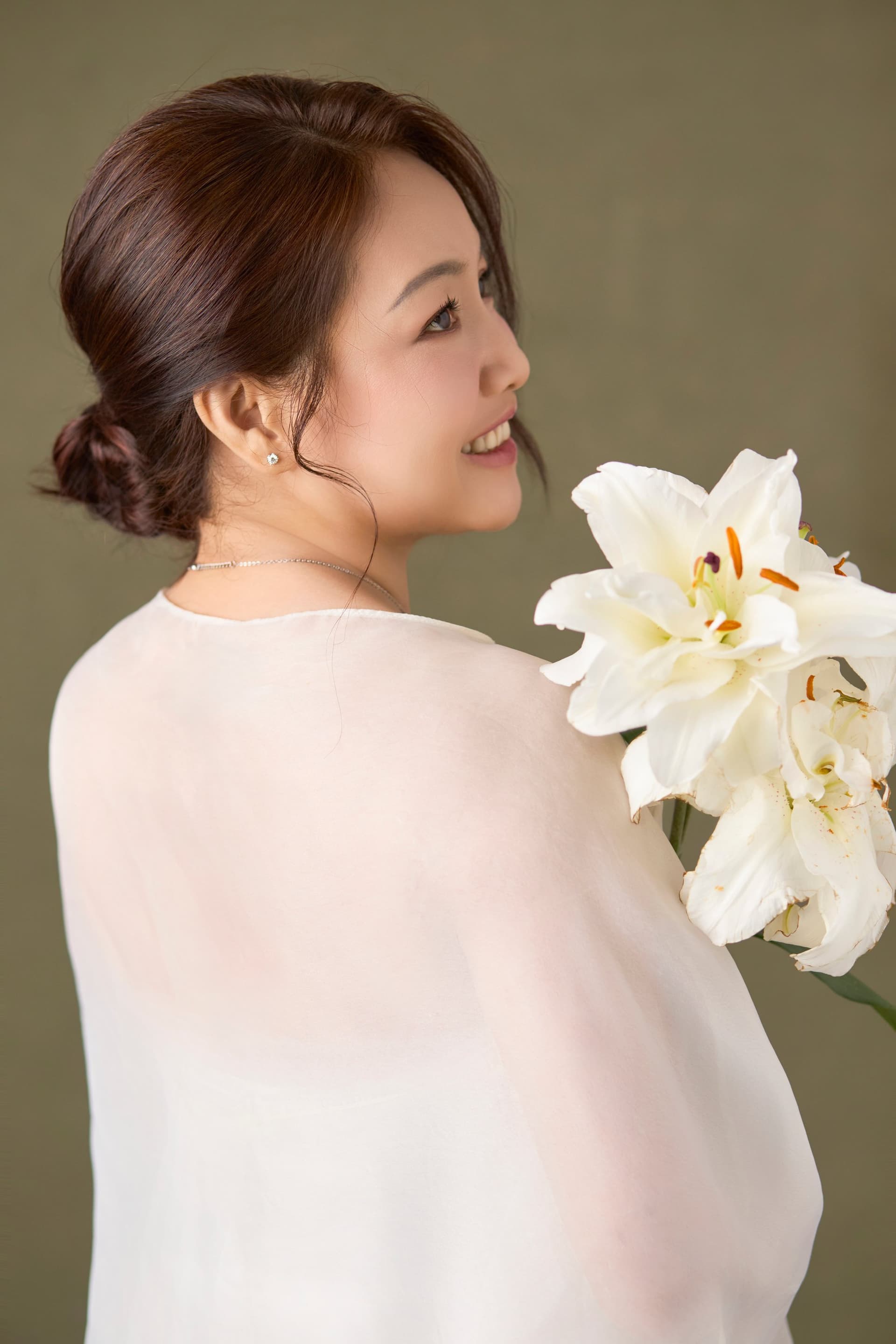 Người phụ nữ năm mươi tuổi, dáng nhìn nghiêng từ phía sau, cầm bó hoa loa kèn trắng, tone đen trắng