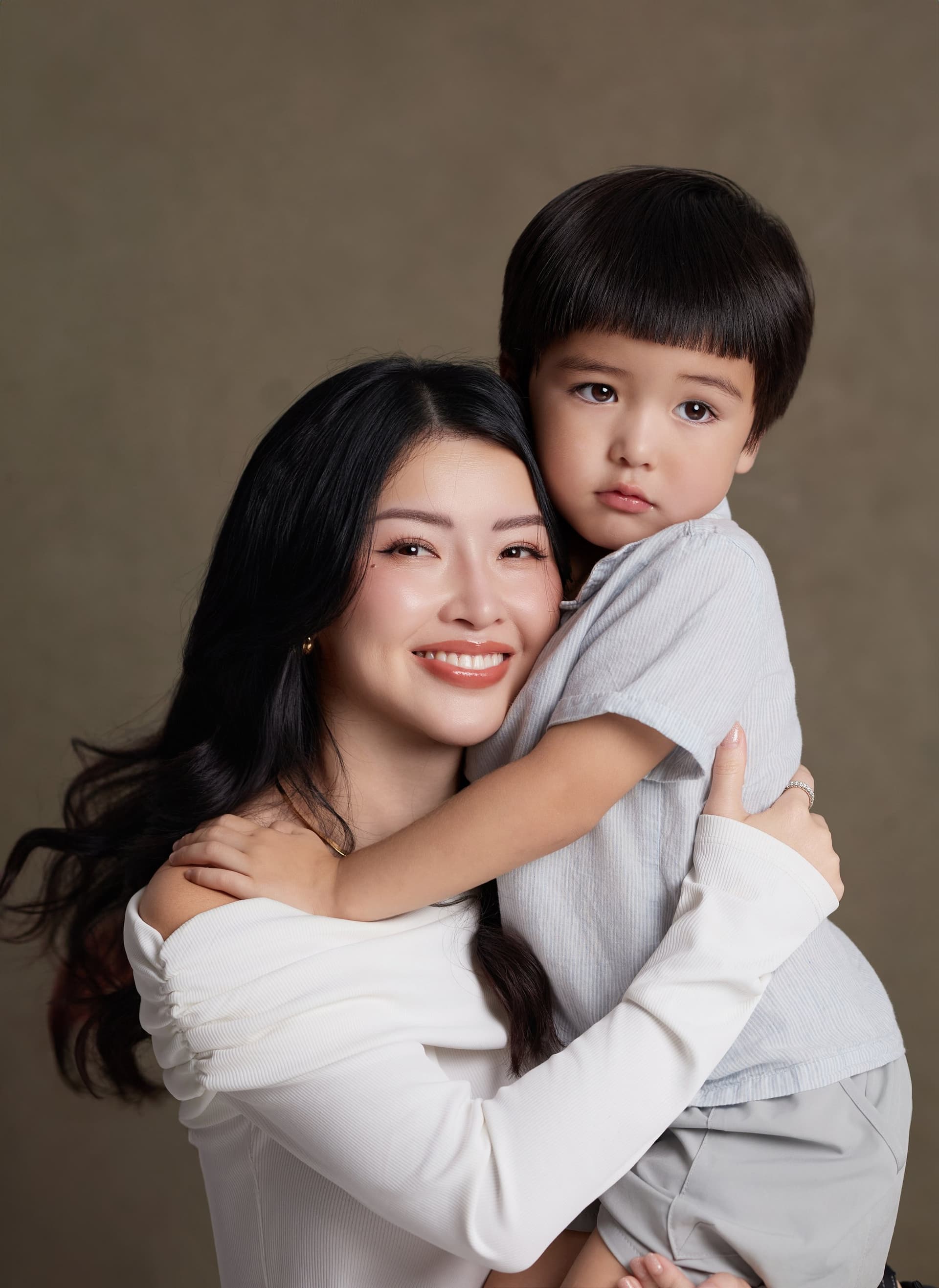 Trang cúi xuống ôm cậu con trai nhỏ vào lòng, hai mẹ con áp sát — một mốc tuổi có thêm người khác ở trong