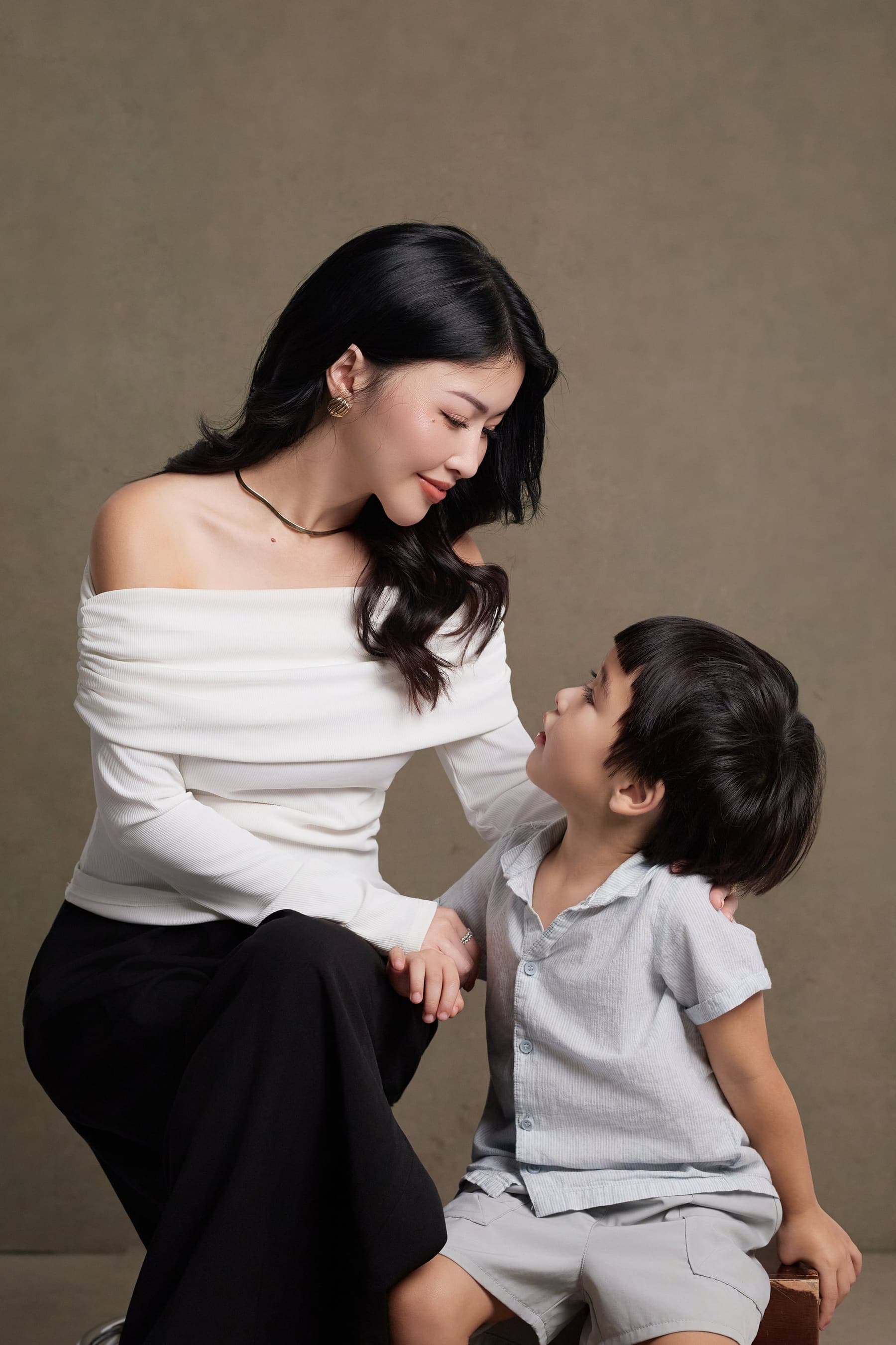 Trang nghiêng người về phía con trai nhỏ, hai mẹ con nhìn nhau, bàn tay con đặt vào lòng mẹ — một phần đời bé xíu đang lớn lên cùng mẹ