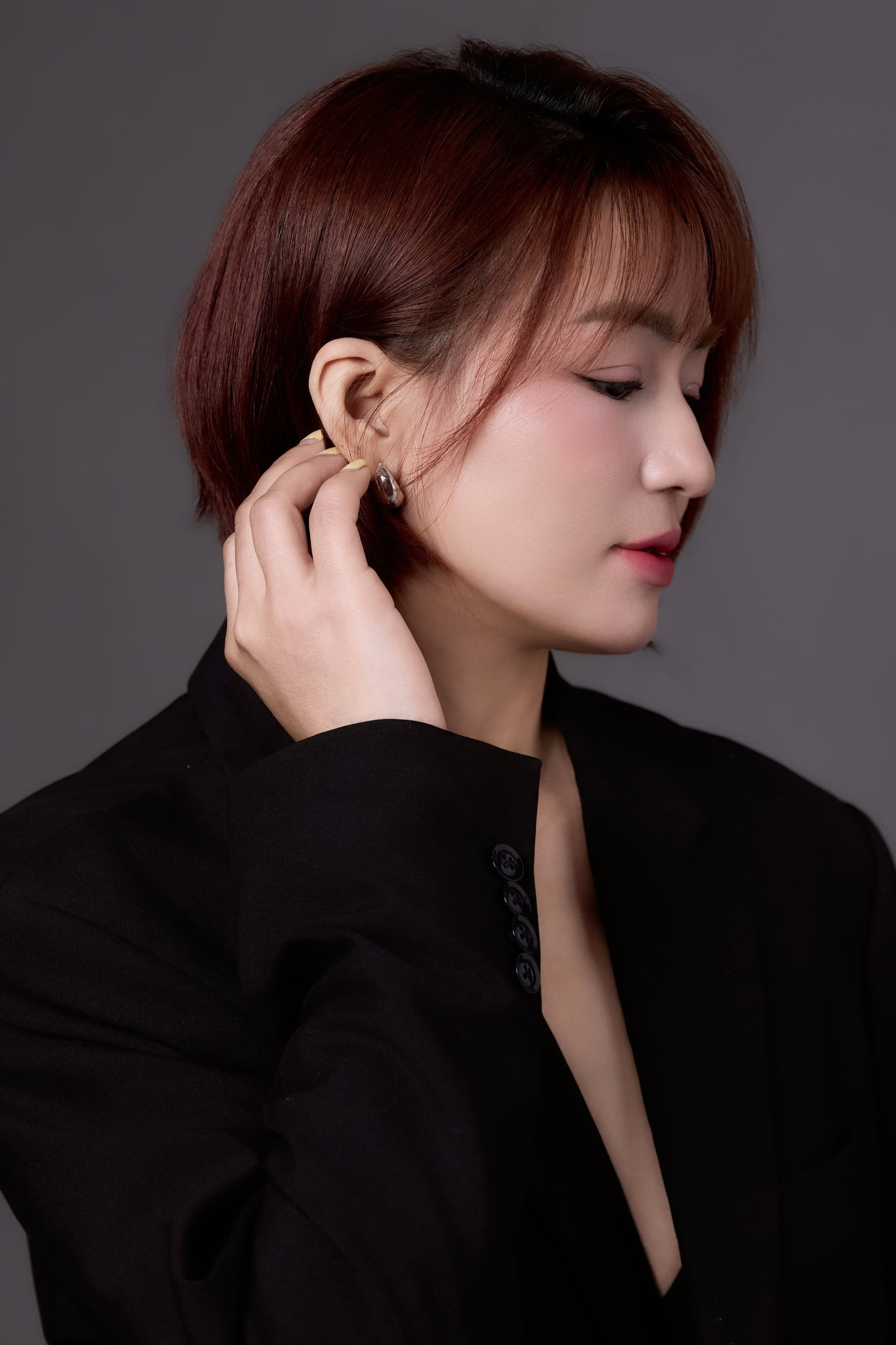 Người phụ nữ trong vest đen, một bàn tay vuốt nhẹ — gương mặt của một người đã nhiều năm xếp mình xuống cuối hàng những việc cần làm