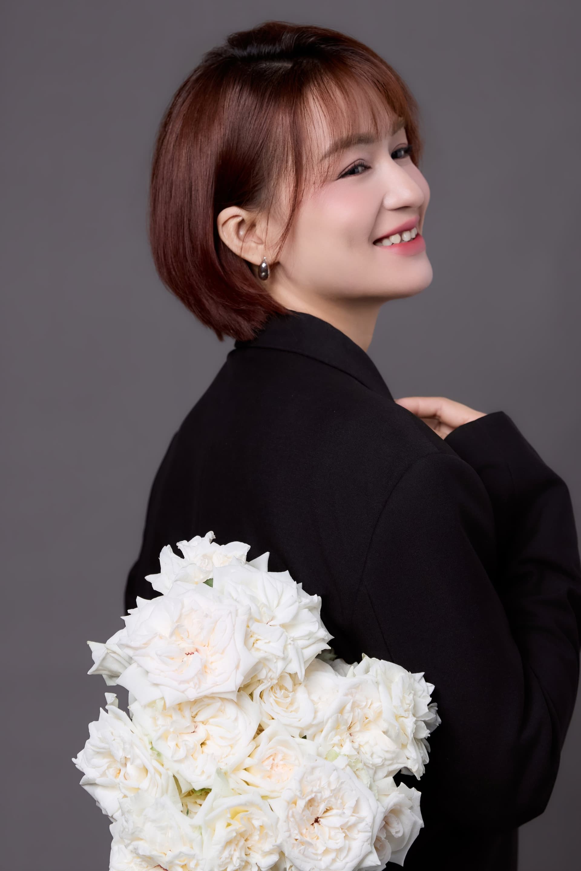 Chị nghiêng người, lưng hơi quay, ôm bó peony trắng dày — dáng của một sự khất dài hai năm với chính mình