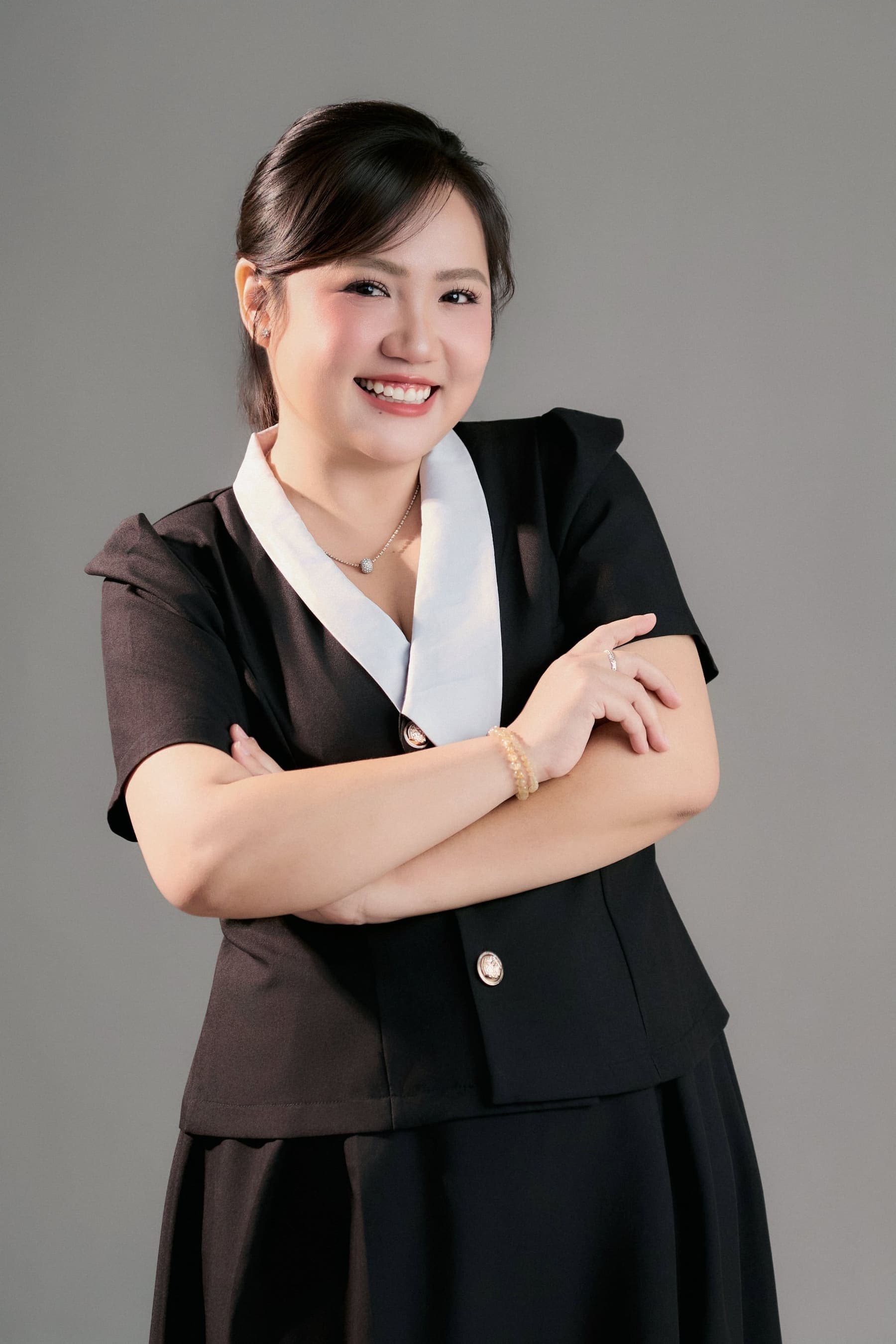 Người phụ nữ vest đen cổ V trắng khoanh tay, cười tươi, ánh nhìn tự tin của một người làm nghề luật