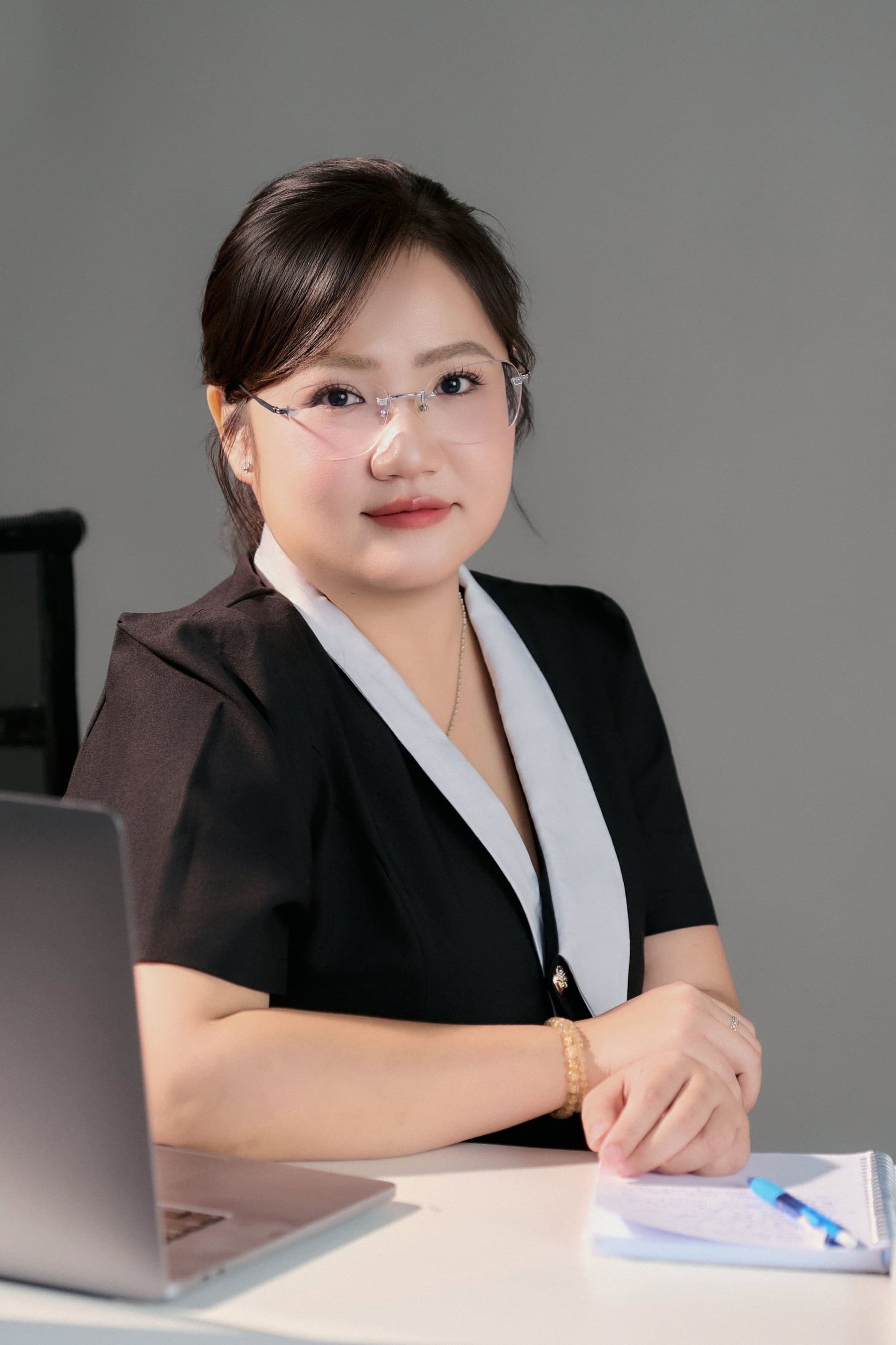 Người luật sư mang kính, ngồi bên bàn làm việc với laptop và sổ tay — ánh nhìn điềm tĩnh, tay đan nhẹ trên bàn