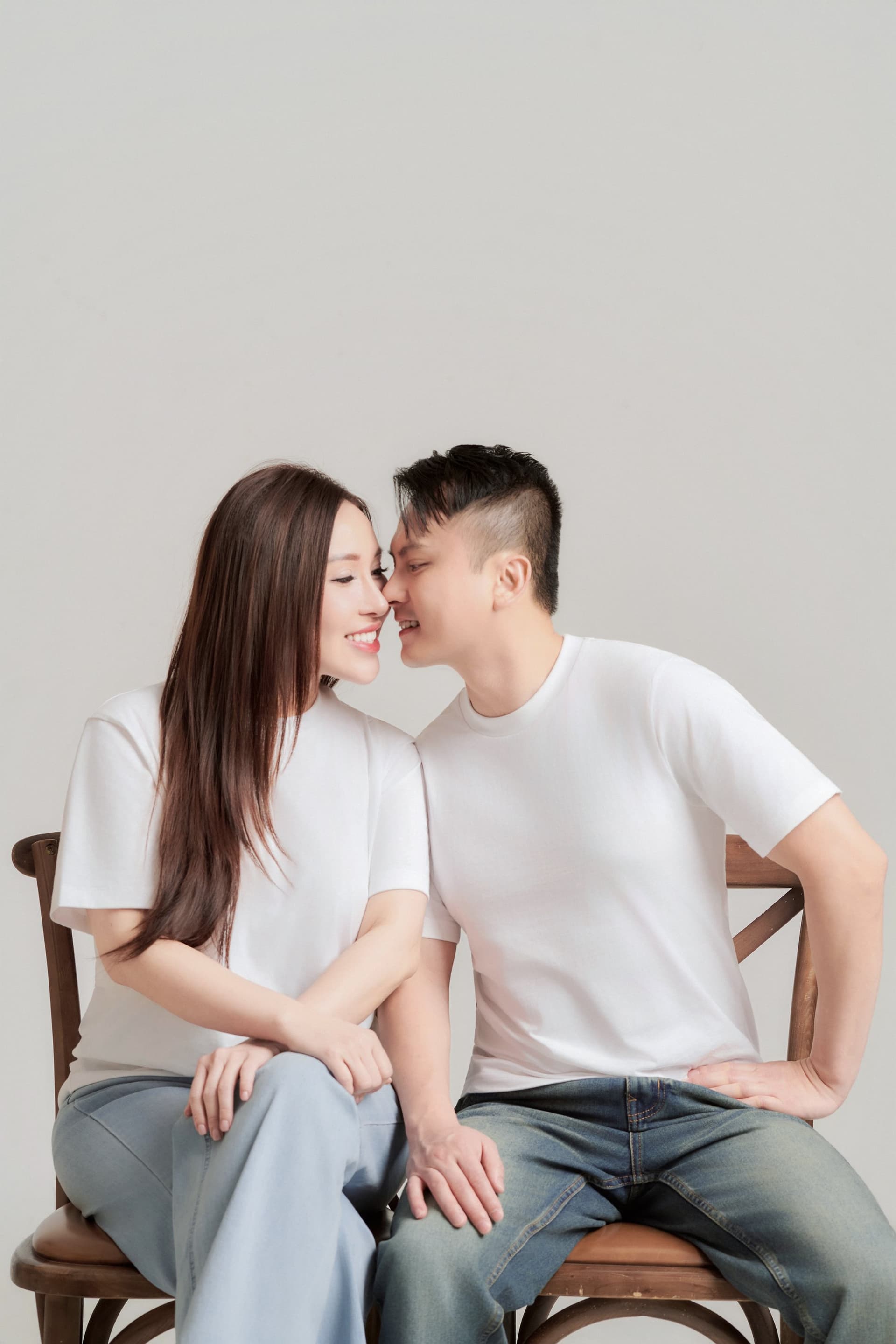 Cặp vợ chồng trẻ ngồi cạnh nhau trên ghế gỗ, anh ôm vai vợ — đời sống gần sau một năm về chung nhà