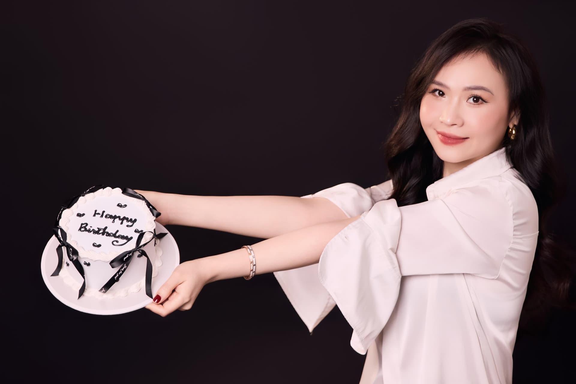 Chị Lý Lưu ngồi mỉm cười rạng rỡ, hai tay nâng niu chiếc bánh kem sinh nhật nhỏ đề chữ Happy Birthday Ly Luu