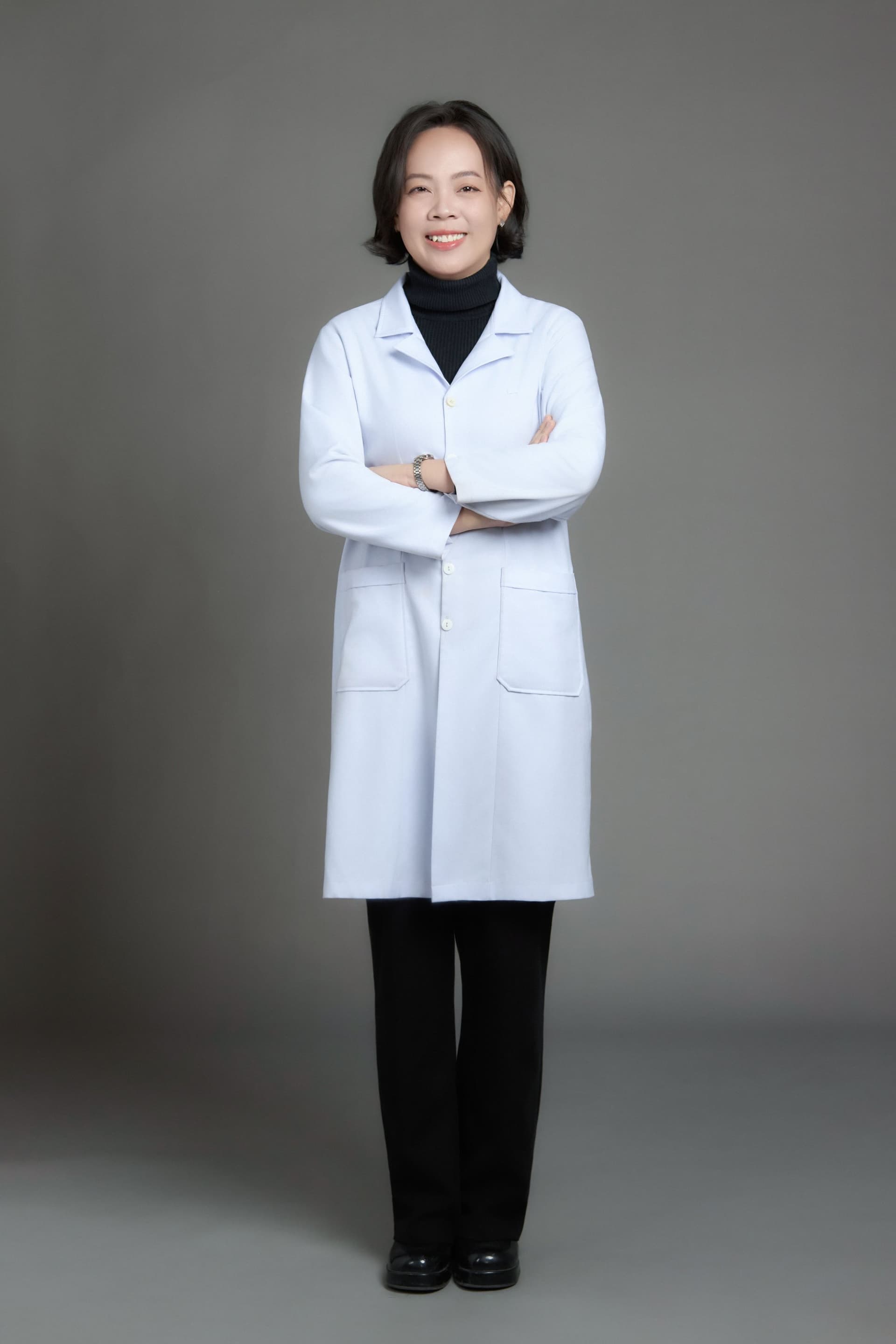 Người phụ nữ mặc áo blouse trắng, đứng thẳng, hai tay khoanh trước ngực, ánh mắt cười nhẹ — một người đã chọn ở lại với nghề