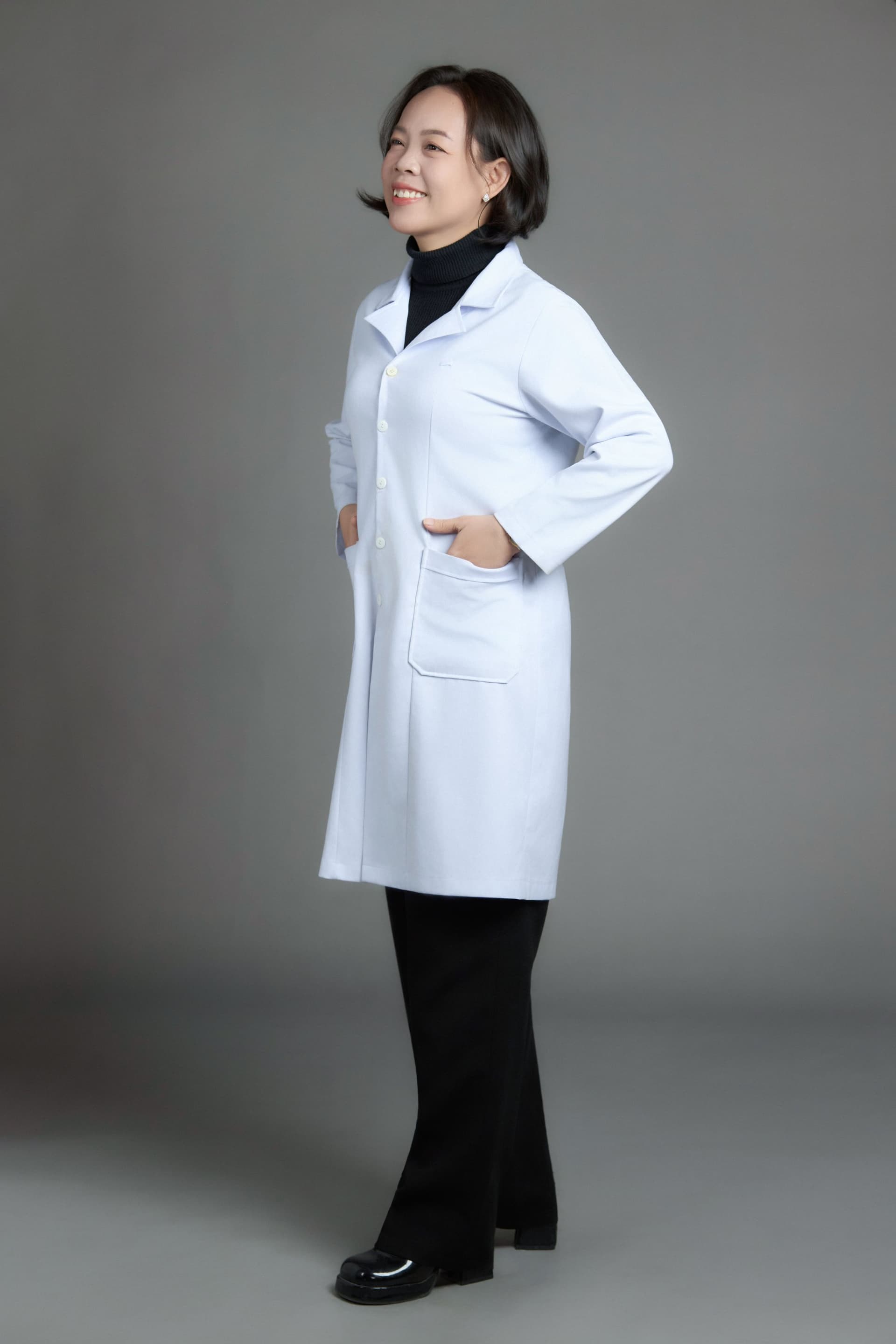 Người phụ nữ ngoài bốn mươi mặc áo blouse trắng, dáng đứng nghiêng, tay vào túi áo — phong thái của một người đã quen với chiếc áo này nhiều năm