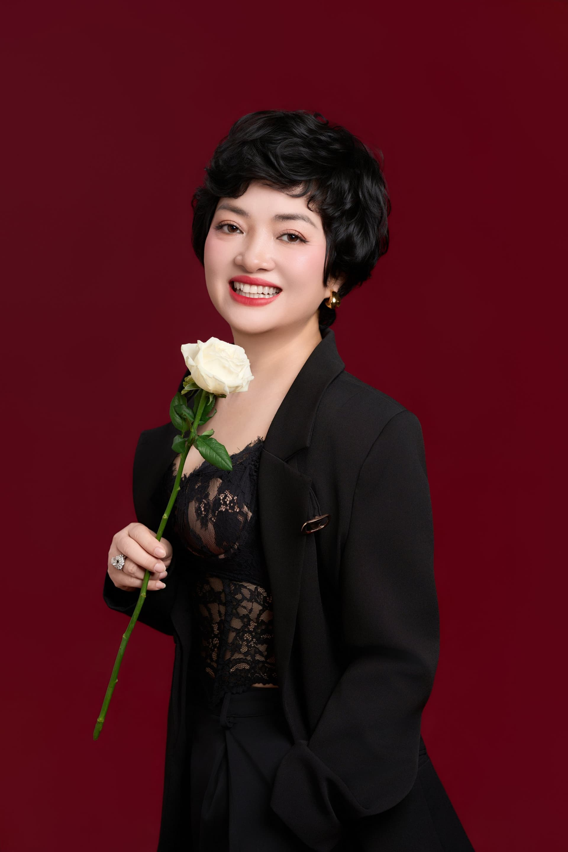 Chị Trần Thị Kim Nhung mặc blazer đen thanh lịch ôm đóa hồng trắng, cười rạng rỡ đầy cá tính