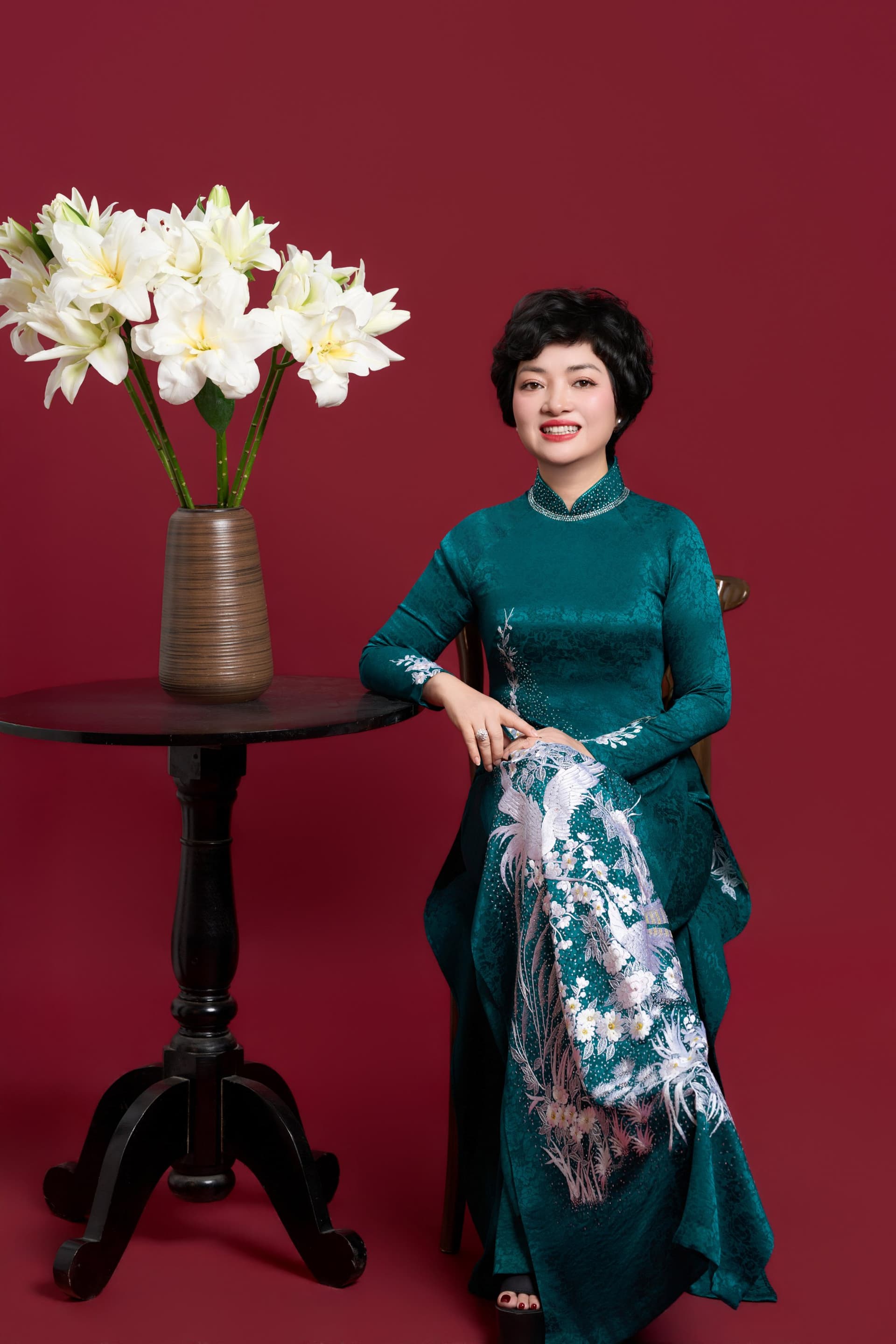 Chị Trần Thị Kim Nhung thướt tha trong tà áo dài xanh ngọc bên bình hoa loa kèn, nụ cười thanh lịch tao nhã