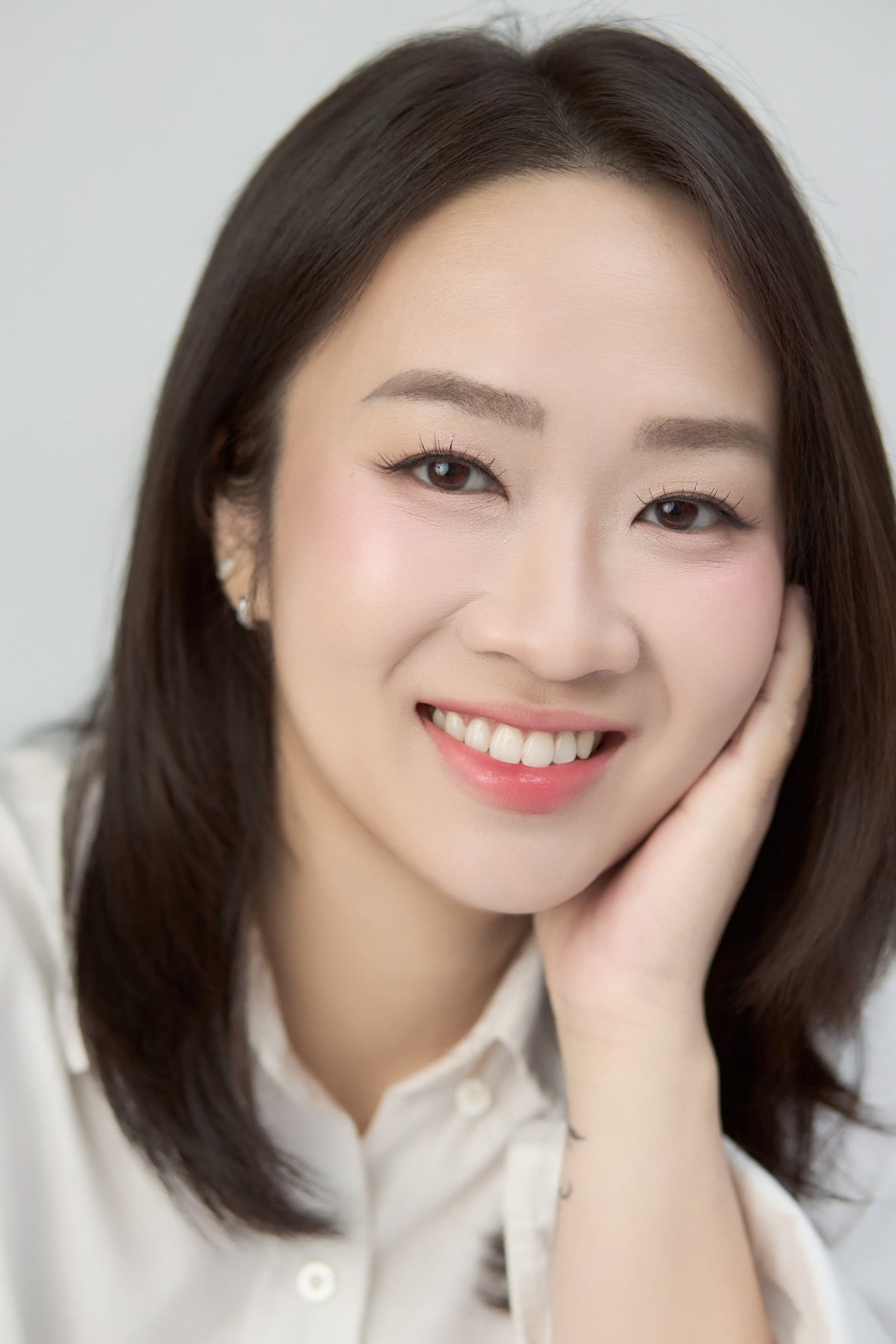 Trần Ngọc Minh Trâm áo sơ mi trắng, một tay đỡ má, nụ cười rạng rỡ — gương mặt của một ngày tự cho phép mình dừng lại