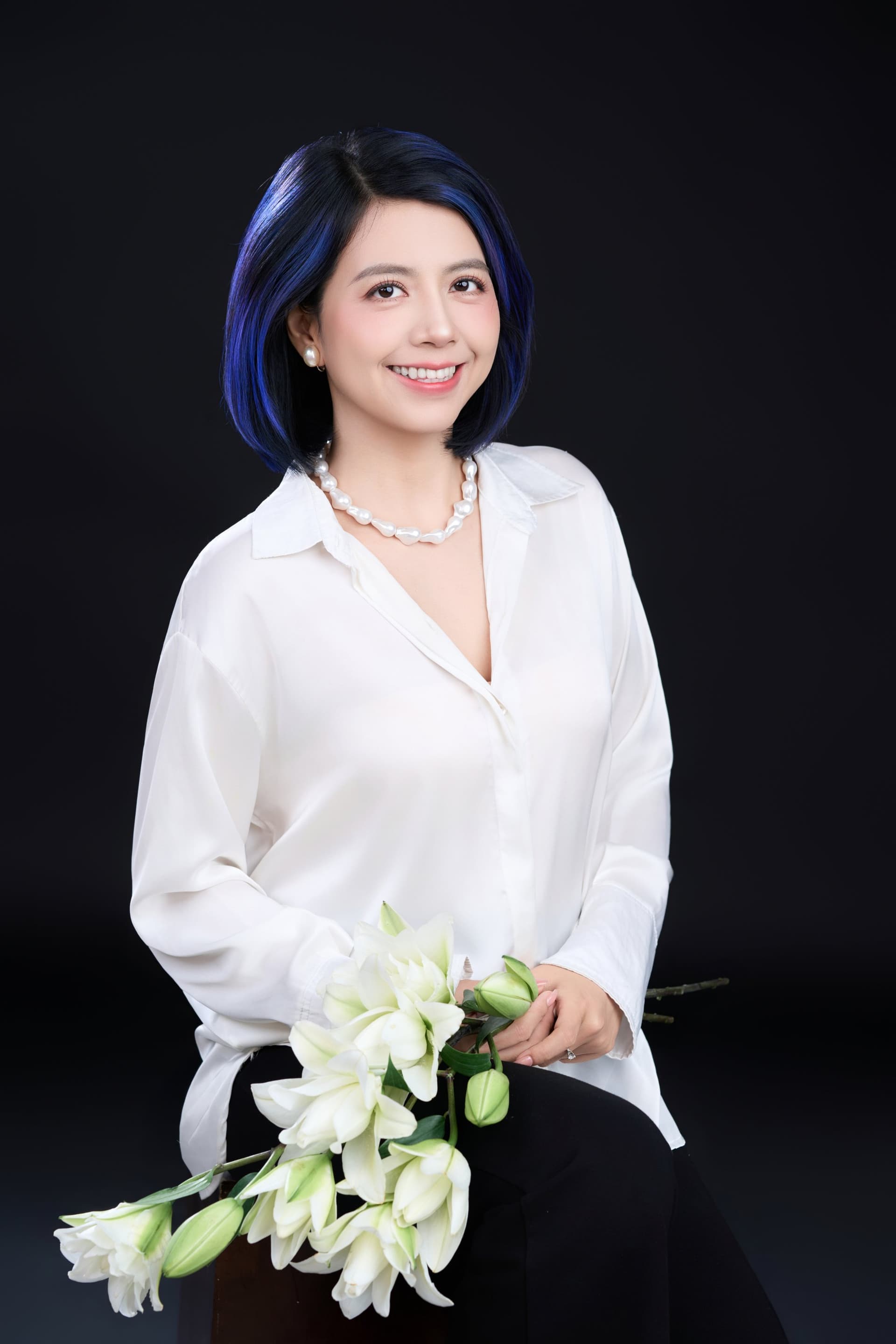 Cô gái áo sơ mi trắng đứng ôm bó hoa lily, dáng nghiêng nhẹ — người phụ nữ chọn một điều cho riêng mình
