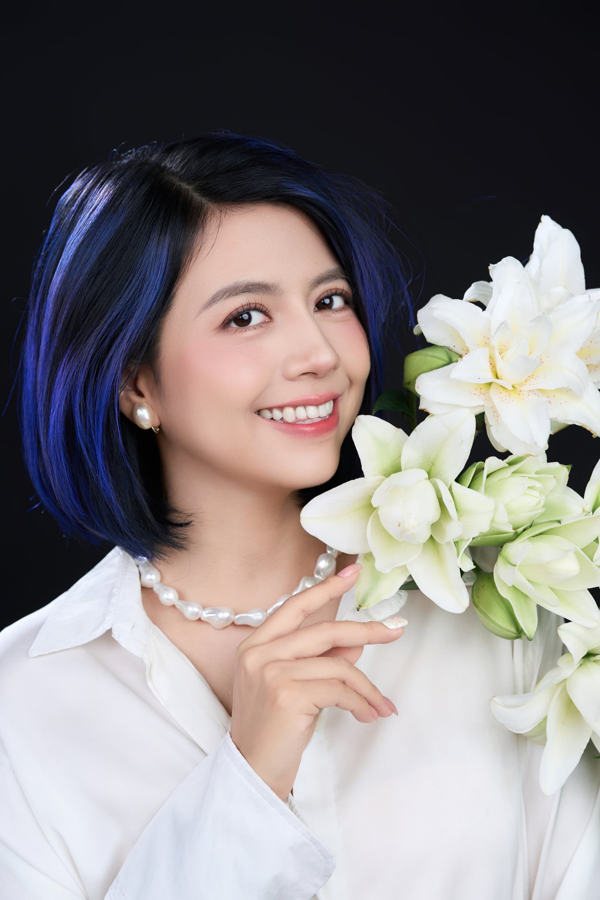Người phụ nữ ngồi ôm bó hoa lily trắng trong lòng, ánh sáng êm trên gương mặt — sự nhẹ nhàng của một người không đặt nặng