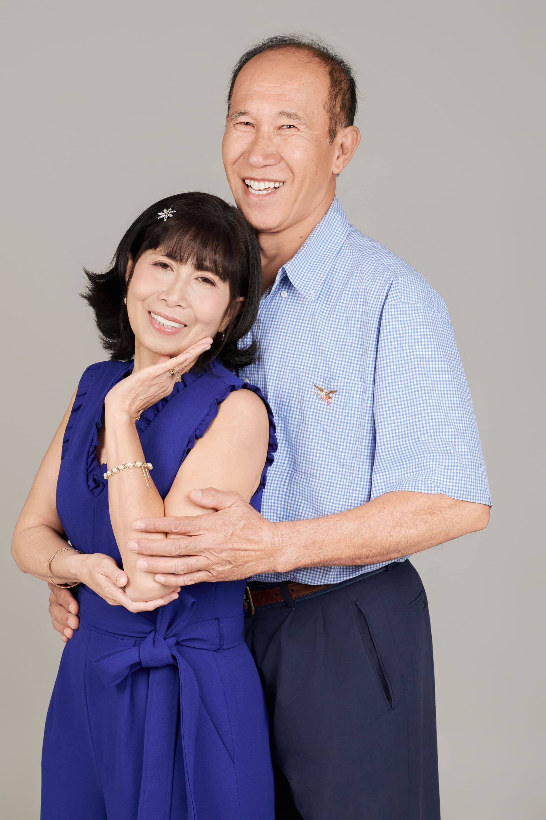 Đôi vợ chồng lớn tuổi ôm nhau dịu dàng, áo sơ mi xanh và áo xanh navy, ánh sáng ấm