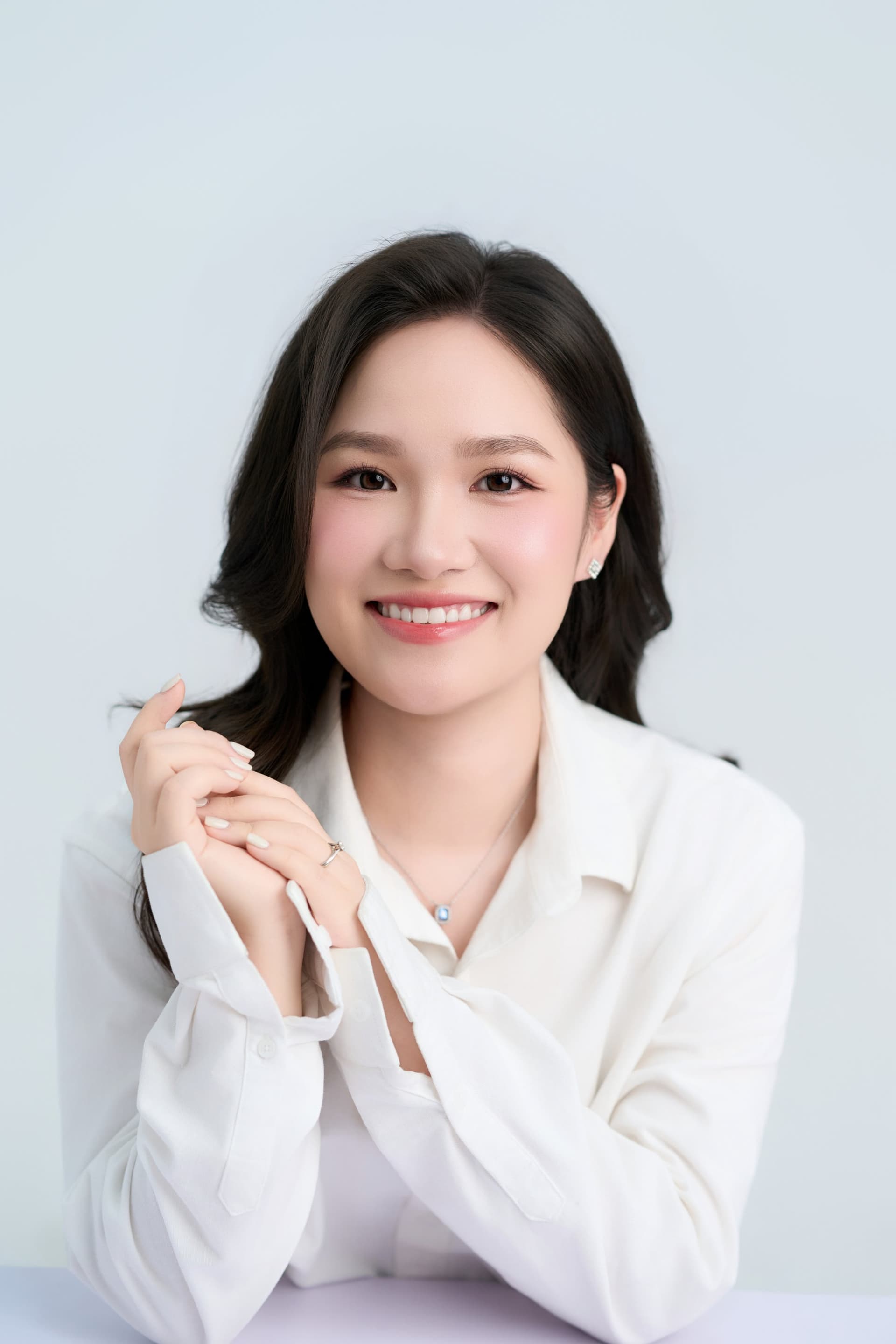 Thu Hà nghiêng đầu cười nhẹ, áo sơ mi trắng, ánh sáng dịu — gương mặt của tuổi đôi mươi còn rất tươi