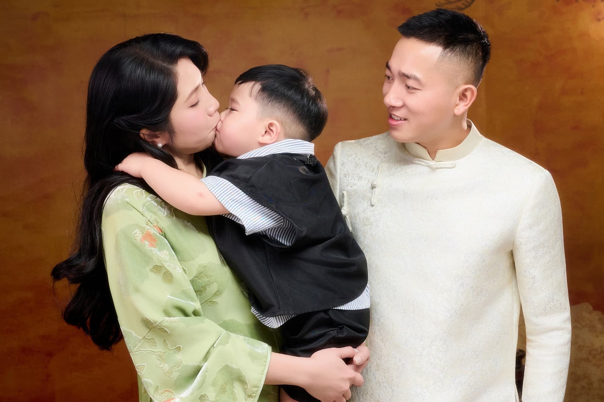Khoảnh khắc cha mẹ áp má, hôn lên má con nhỏ — cả nhà chụm vào nhau trong một khung hình ngang