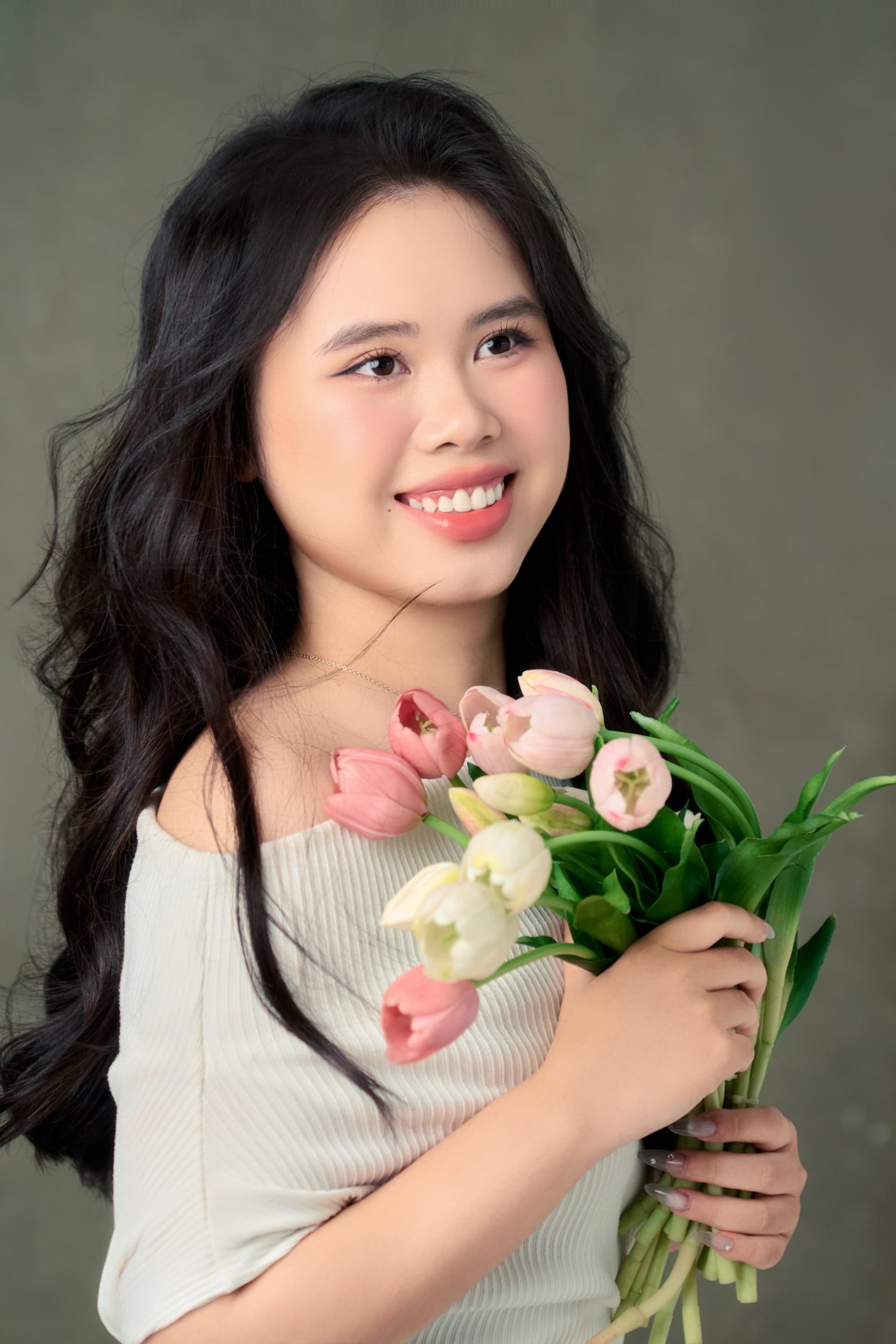 Cô gái áo trắng ôm bó tulip phấn, nụ cười sáng trong ánh sáng dịu — khoảng lặng tháng Năm trước sinh nhật