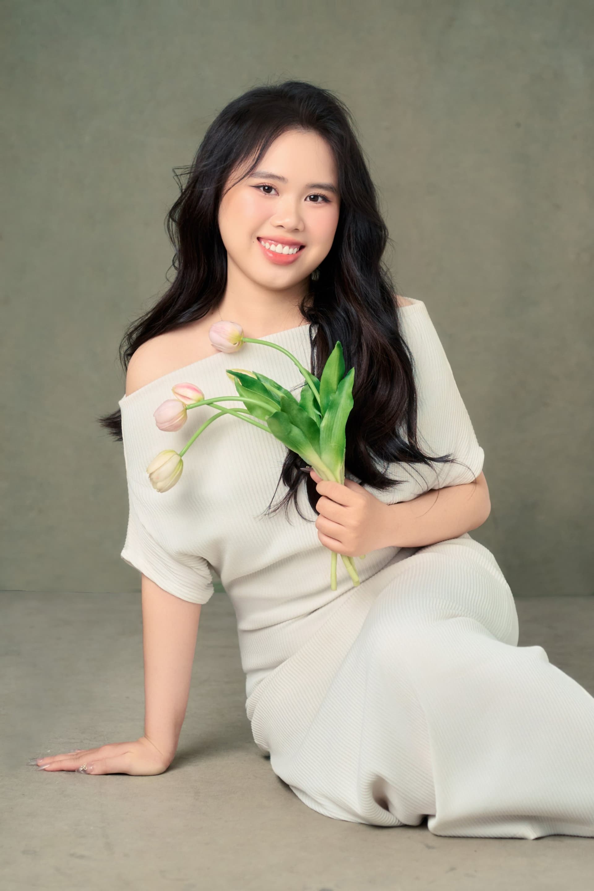 Cô gái ngồi nhẹ với bó hoa trên tay, dáng dịu trong gam sage — vẻ mạnh mẽ theo cách riêng, không cần làm rộn