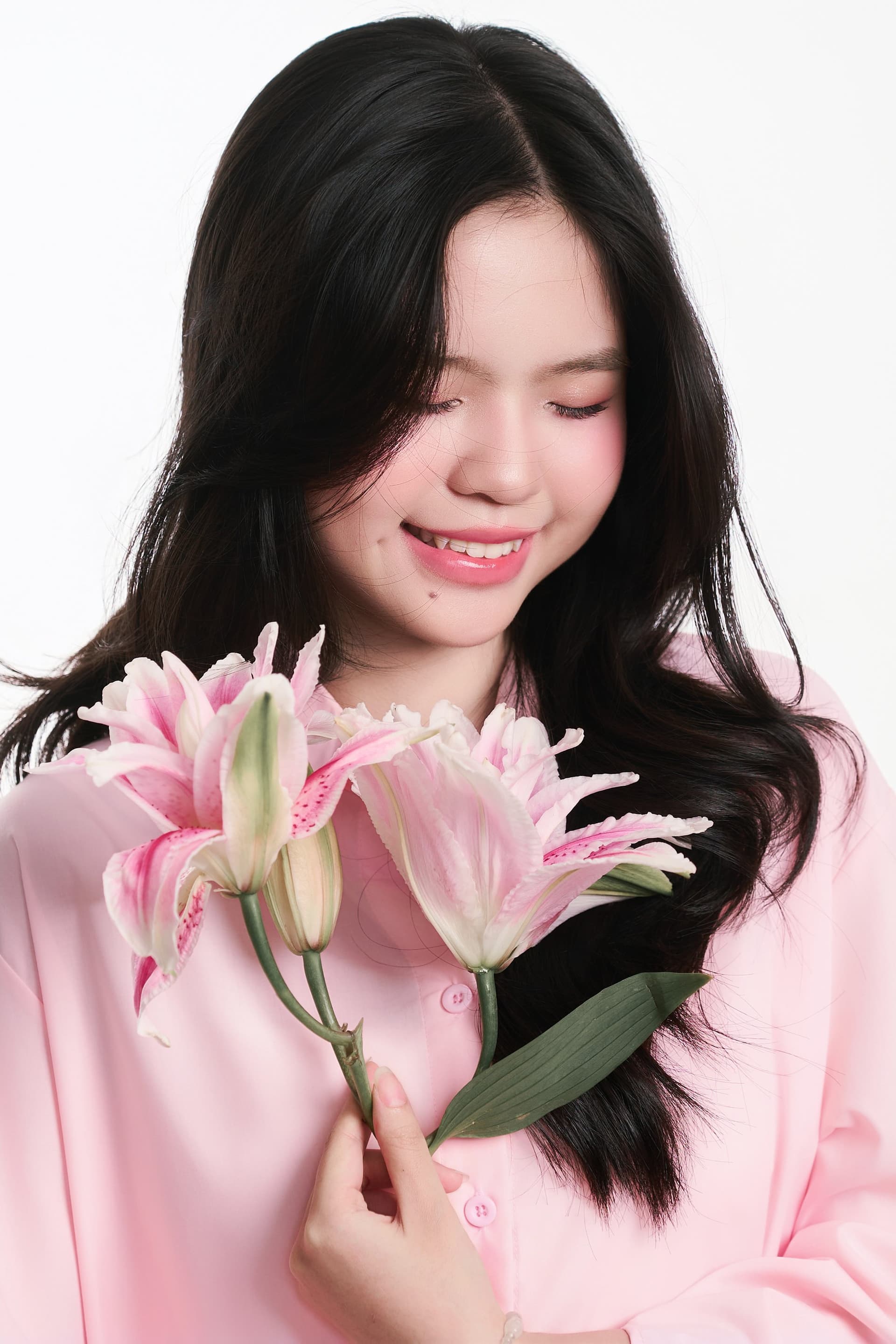 Cô gái trẻ mặc áo sơ mi hồng nhạt nhắm mắt nhẹ nhàng ôm đóa hoa ly hồng trước ngực
