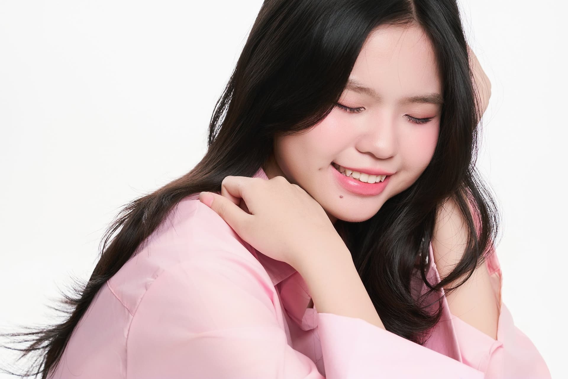 Cô gái tựa cằm vào bàn tay, mái tóc đen dài xõa nhẹ trên vai, cười dịu dàng dưới nắng