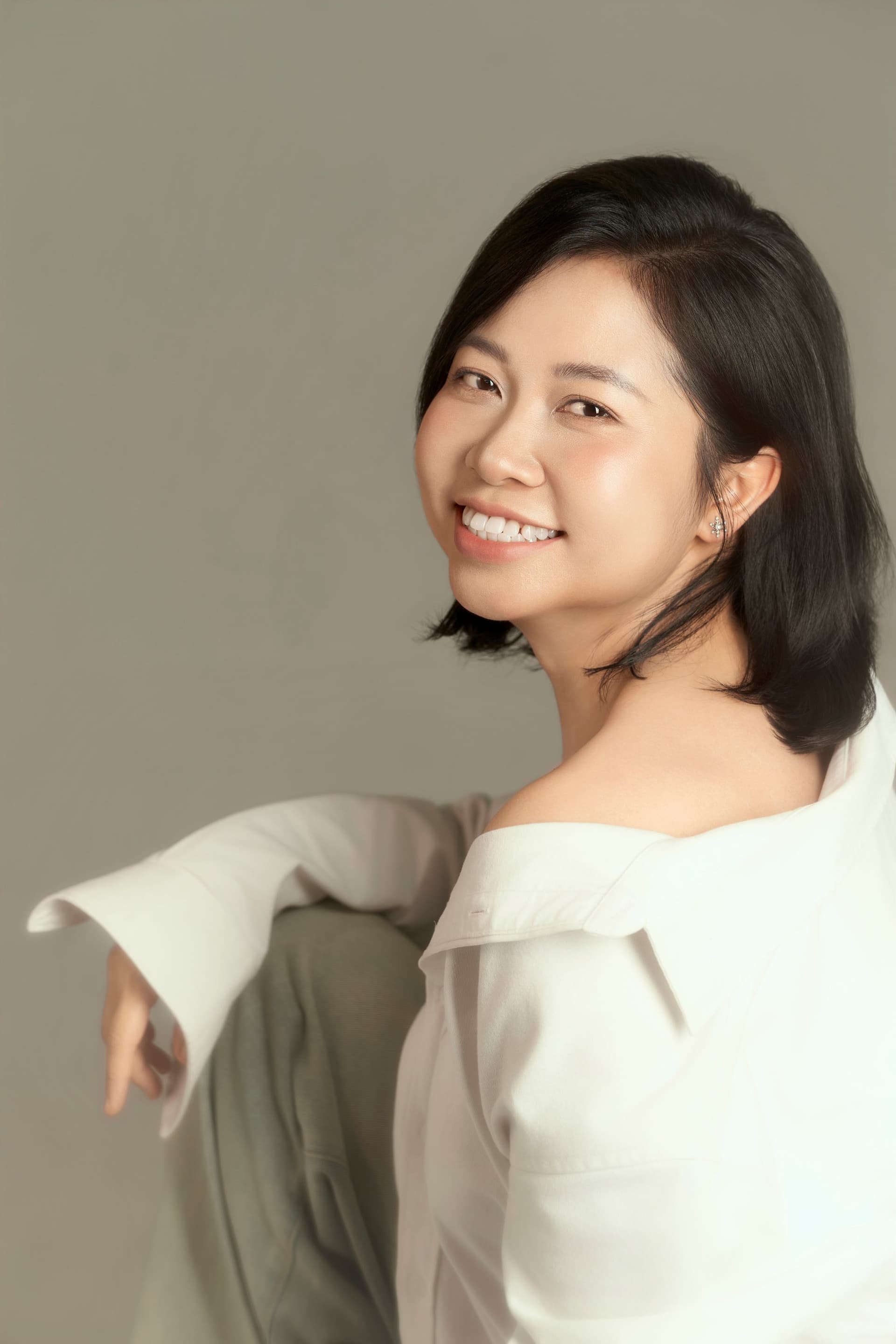 Người phụ nữ ngồi tựa, ngón tay khẽ che một bên mặt, áo trắng — dáng ngồi quen của người đã sống cho người khác quá lâu