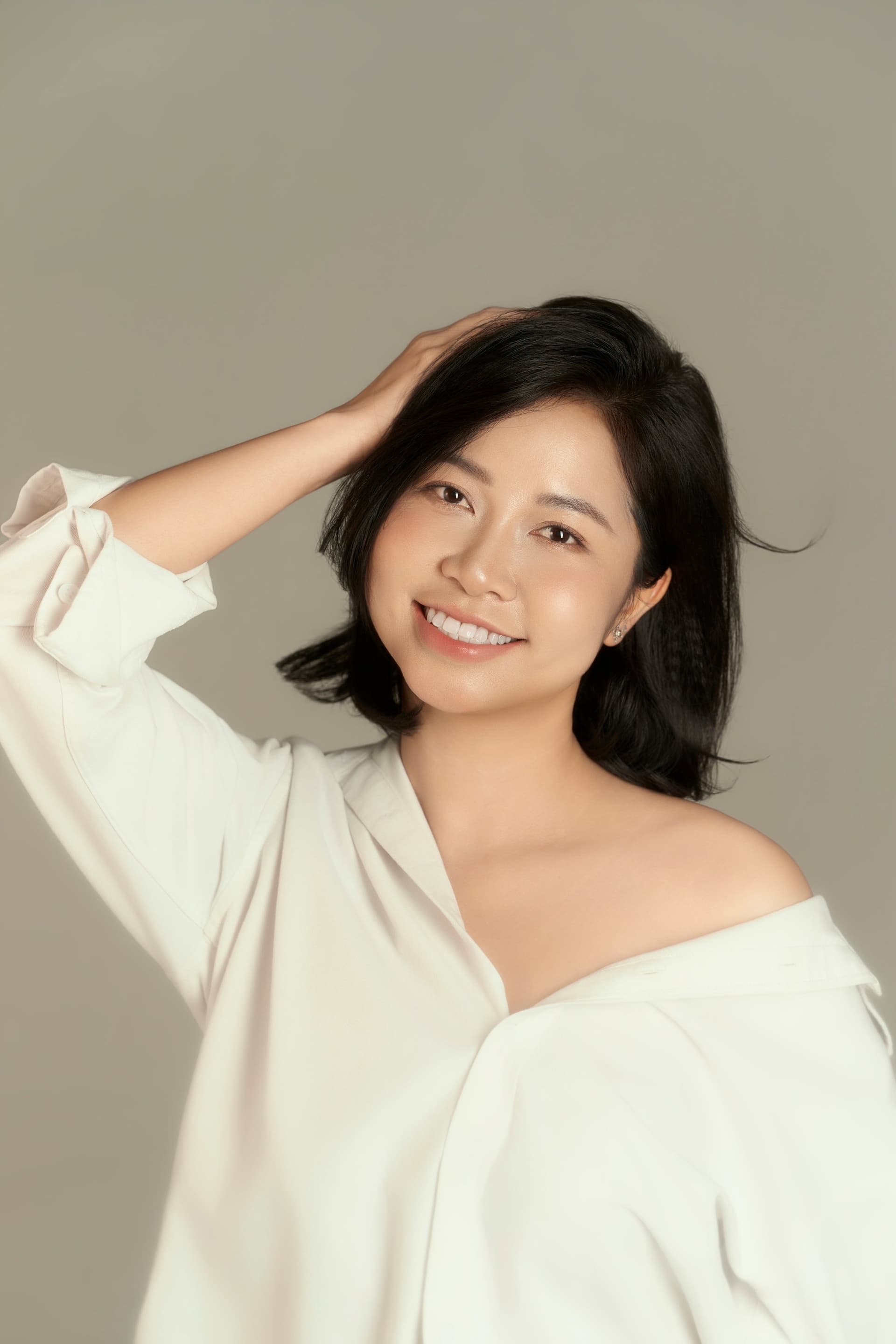 Người phụ nữ vuốt nhẹ mái tóc, áo trắng off-shoulder — một dáng đứng cho riêng mình, không phải cho ai cả
