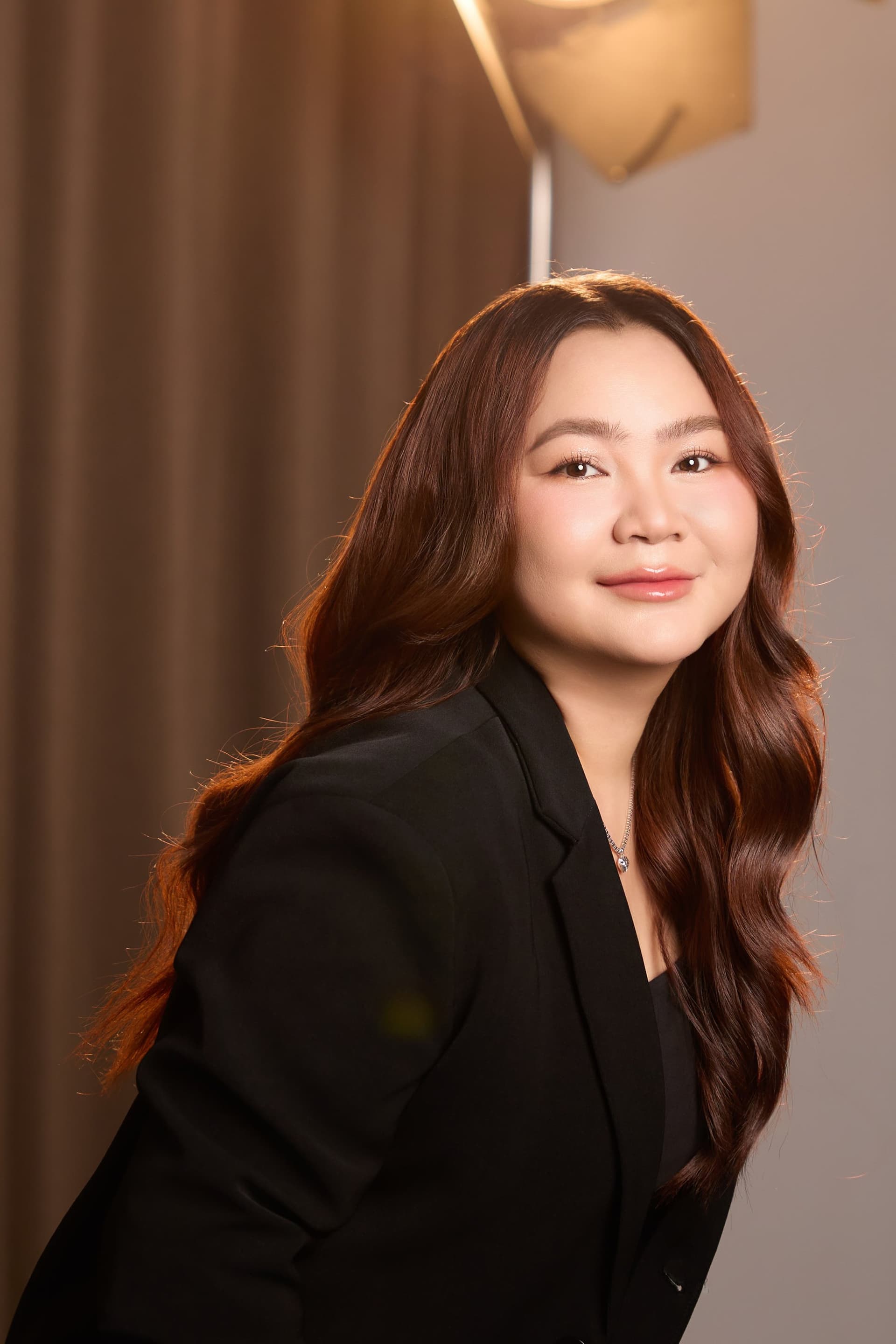 Chân dung chị Lily Nguyen cười nhẹ nhàng, mặc áo blazer đen, mái tóc xoăn dài bồng bềnh.