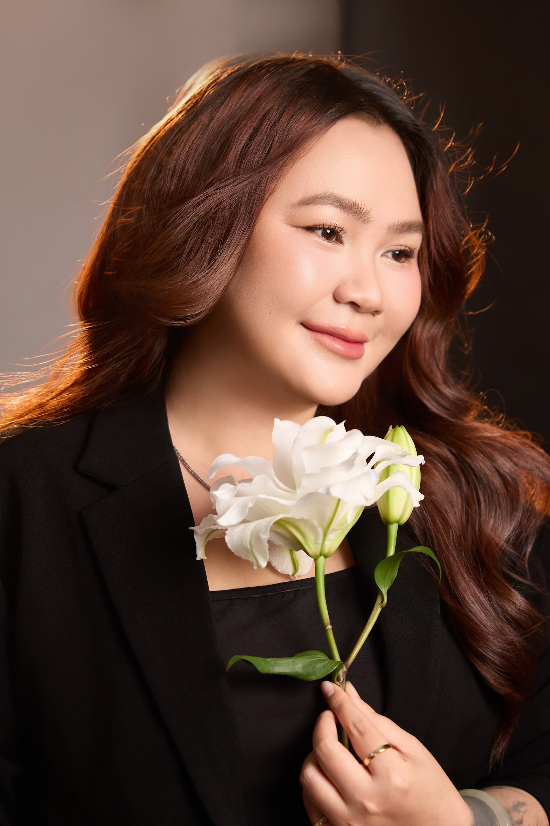 Lily Nguyen cúi đầu mỉm cười nhẹ nhõm, tay nâng niu cành hoa huệ trắng tinh khiết.