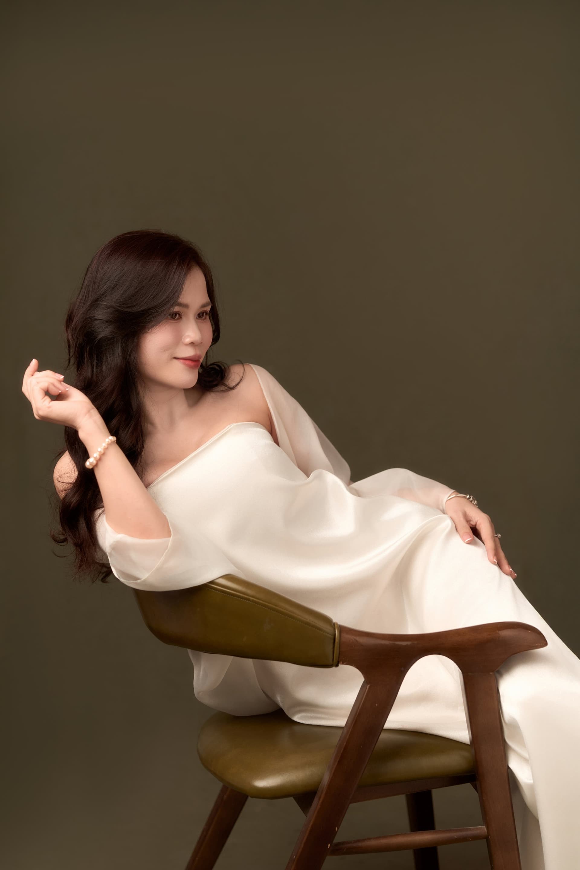 Người phụ nữ áo trắng tựa khẽ vào ghế gỗ, gương mặt buông lỏng — Mai Hương thử dịu, thử mềm trong tuần sinh nhật