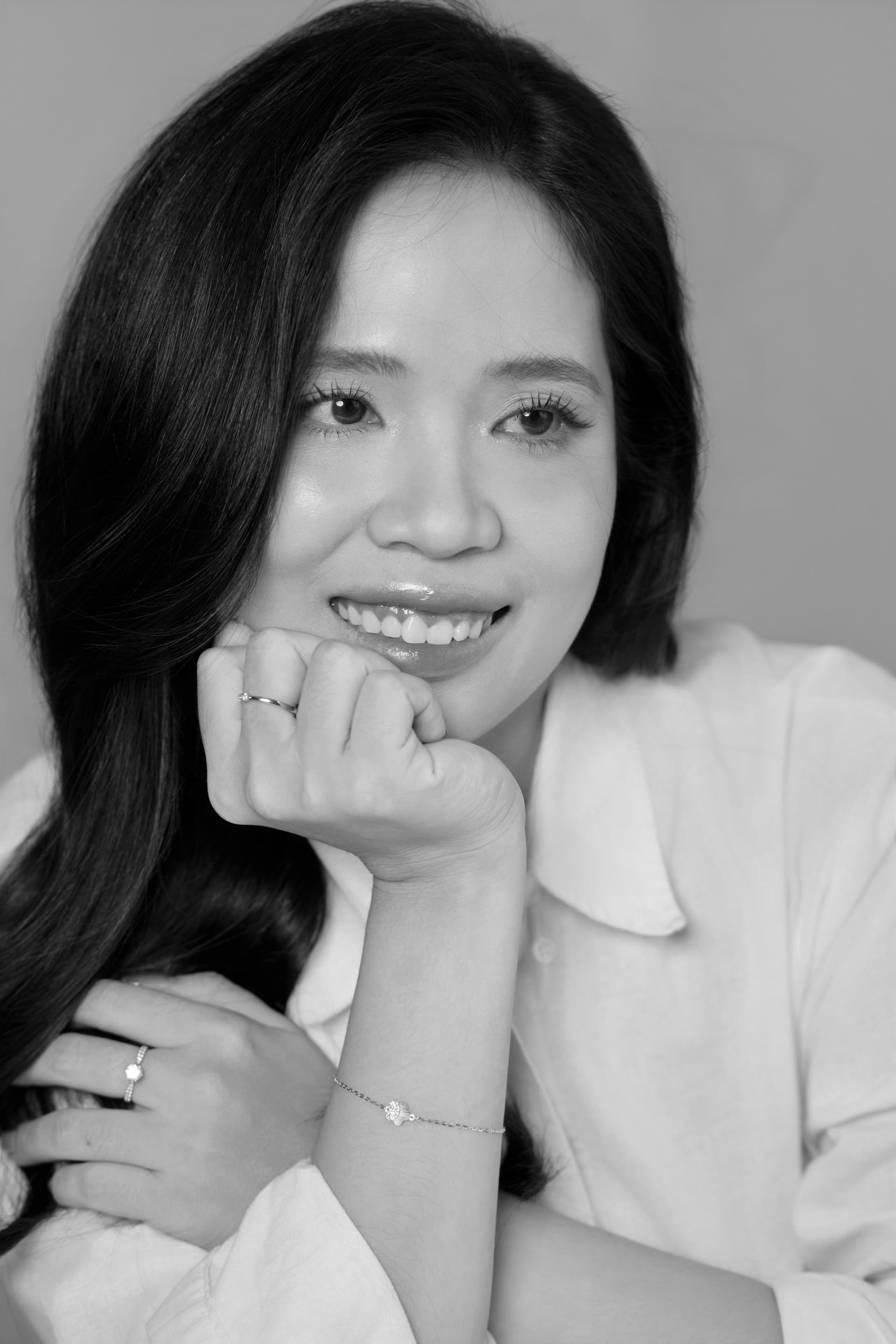 Khung đen trắng, người phụ nữ chống cằm lên bàn tay, ánh mắt dịu lại — khoảnh khắc của một người đang tự đặt cho mình một câu hỏi quan trọng.