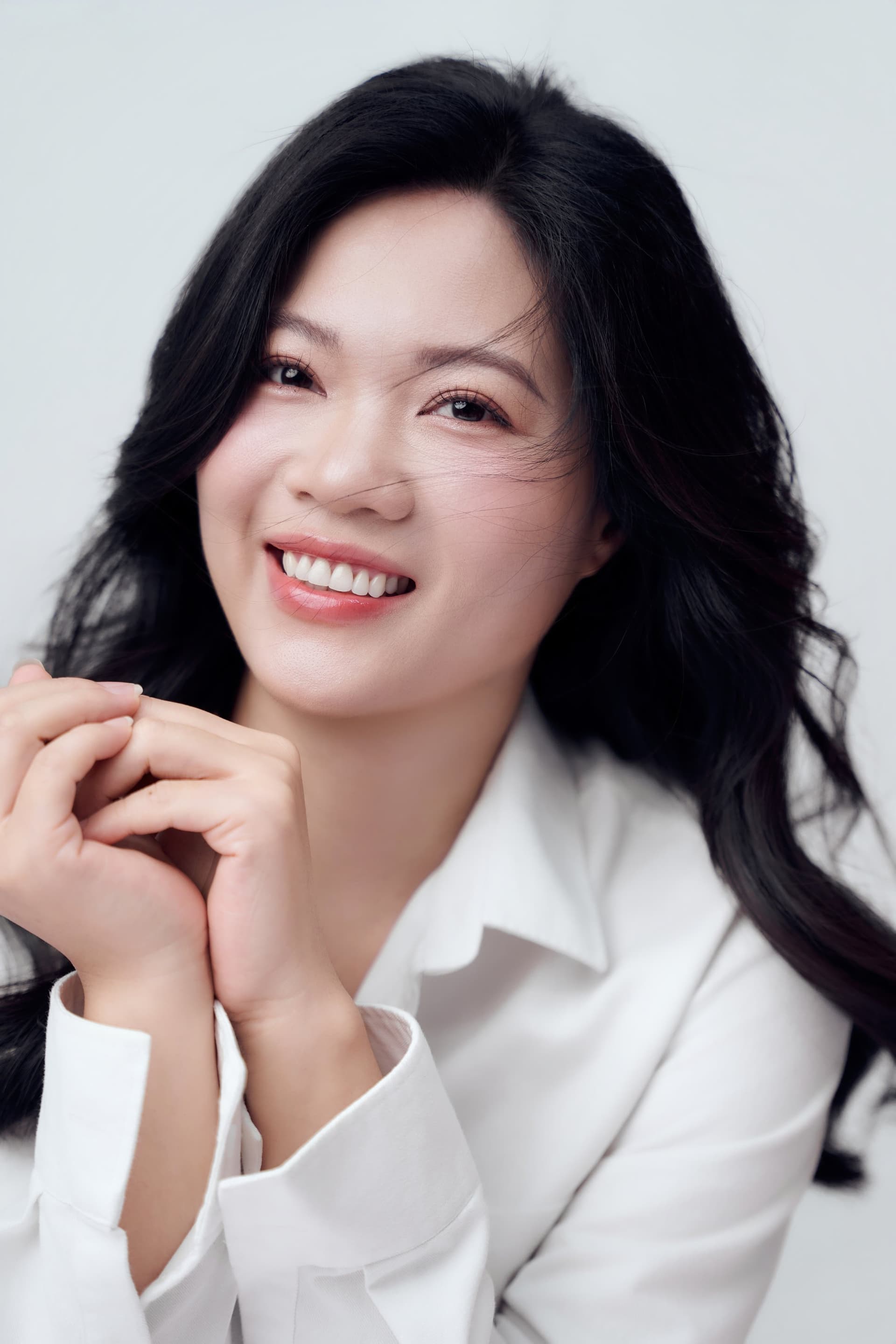 Phi Hiền nở nụ cười rạng rỡ đan hai tay trước ngực, nét cười tự nhiên và ấm áp