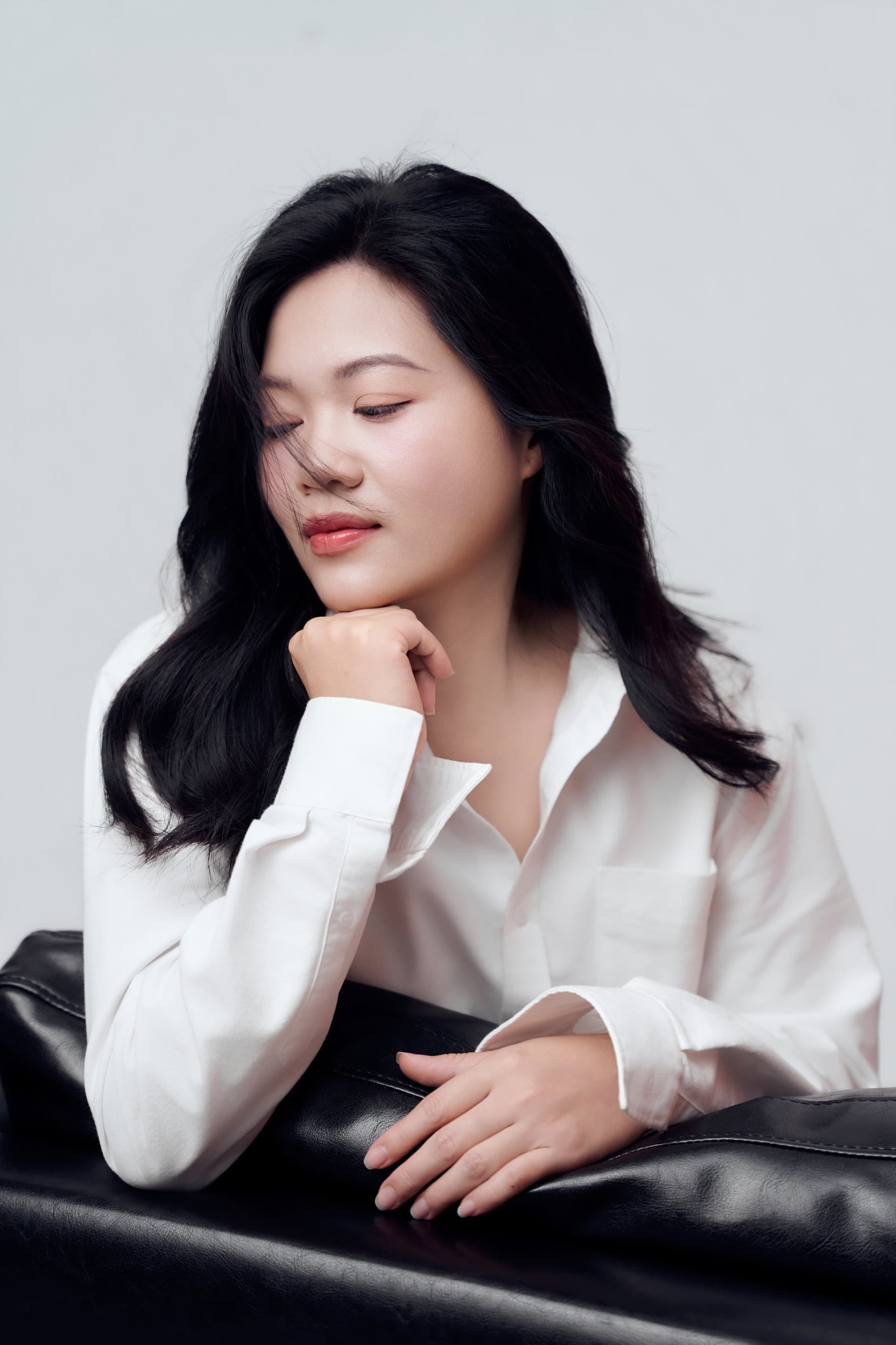 Phi Hiền ngồi trầm ngâm trên chiếc ghế da đen, ánh mắt nhìn xuống nhẹ nhàng và sâu lắng