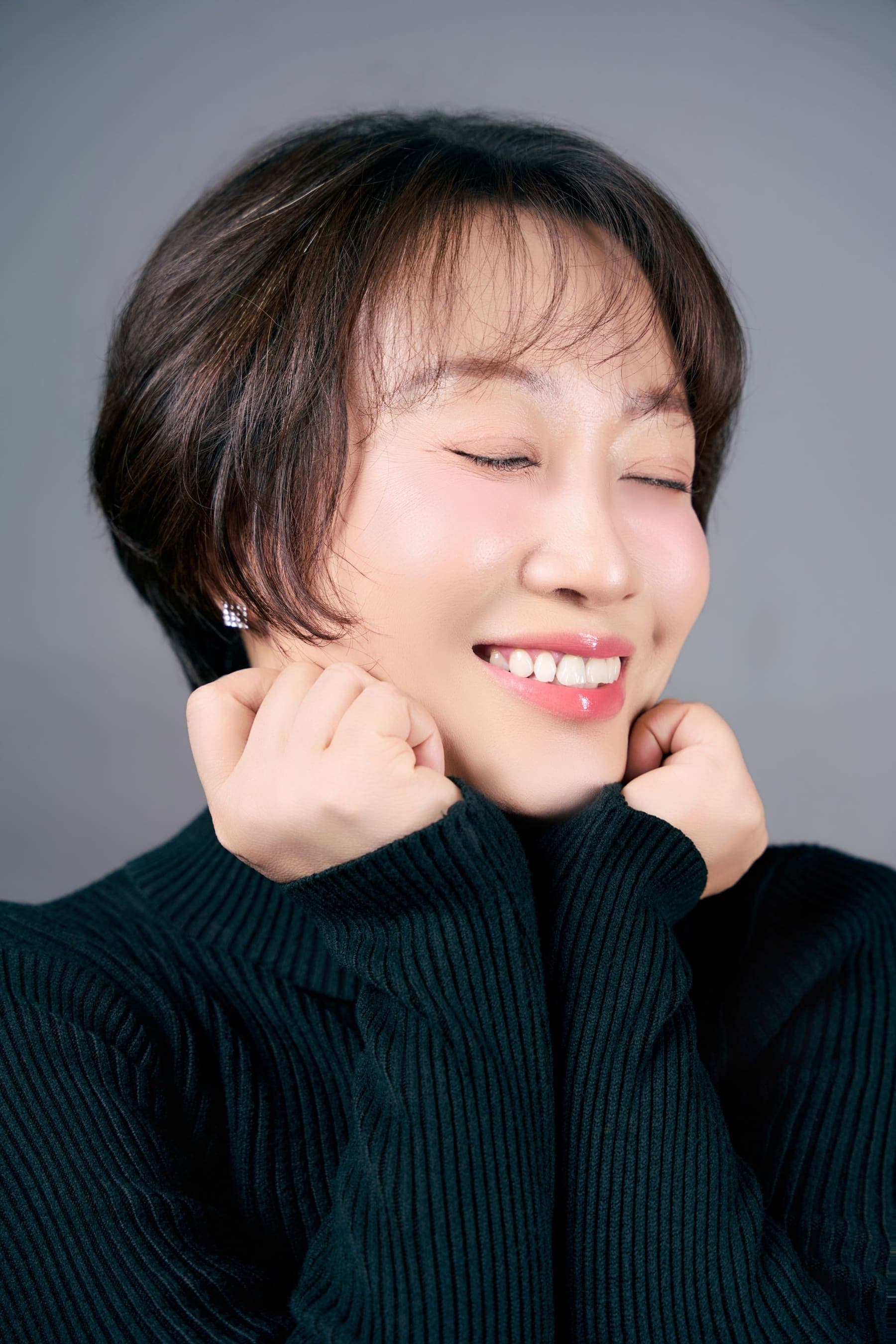 Người phụ nữ tóc ngắn áo đen cao cổ, một bàn tay đỡ nhẹ cằm, gương mặt của người đã đi qua nhiều mùa và biết rõ giá trị của một sáng dành riêng cho mình