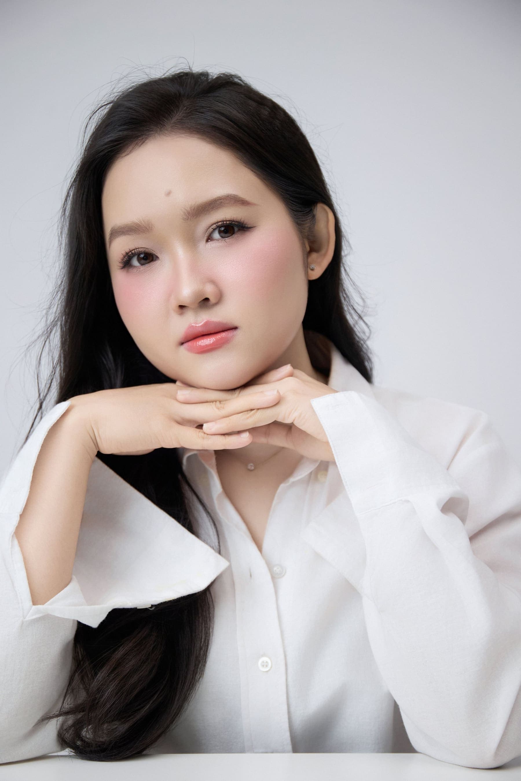 Người phụ nữ trẻ ngồi nghiêng, ánh nhìn xa xăm, một mình giữa nền sáng, mang theo nét trầm của tuổi đang bắt đầu chín
