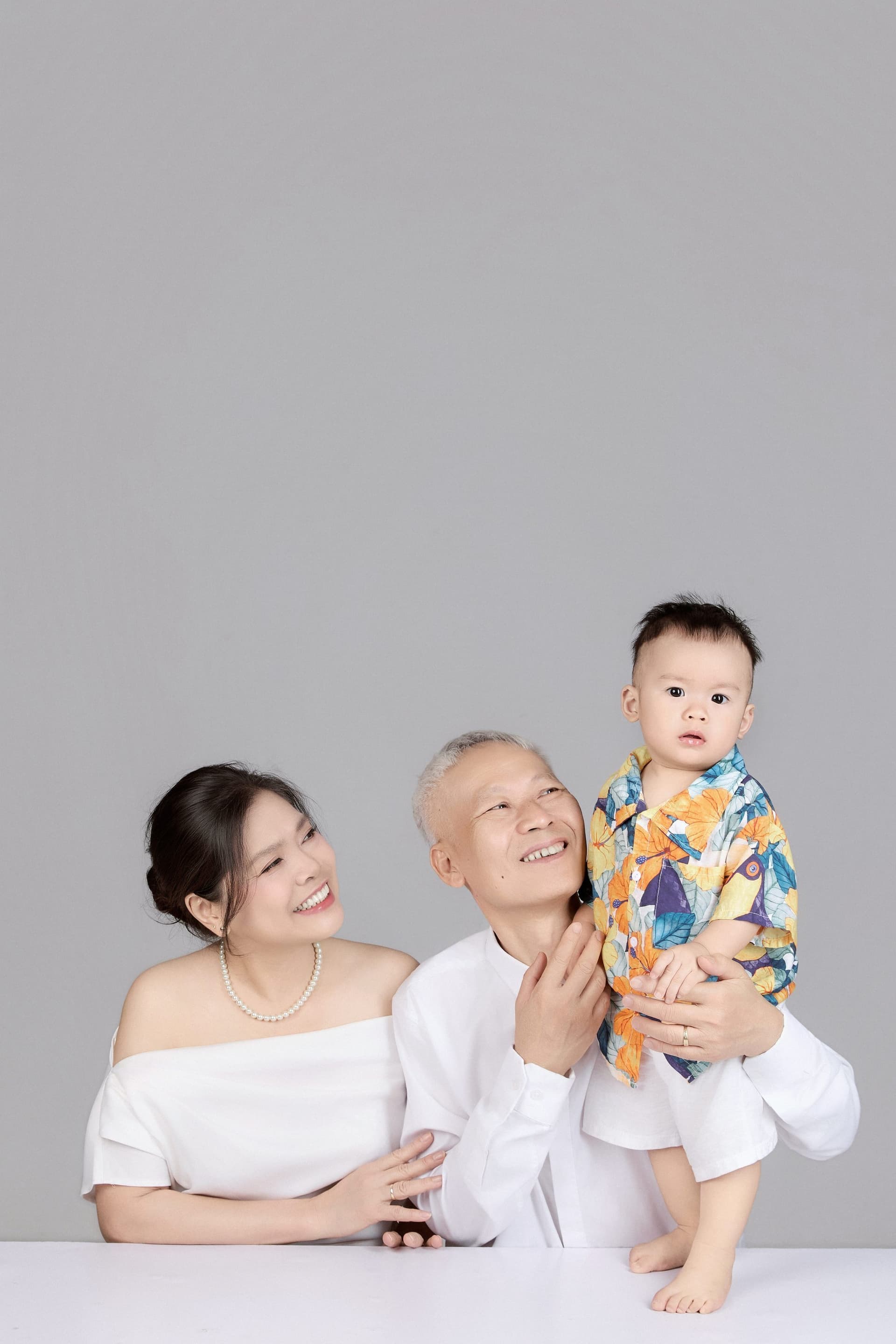 Ông tóc bạc nâng em bé bằng sự chậm rãi và nâng niu của tình yêu thương bên cạnh bà