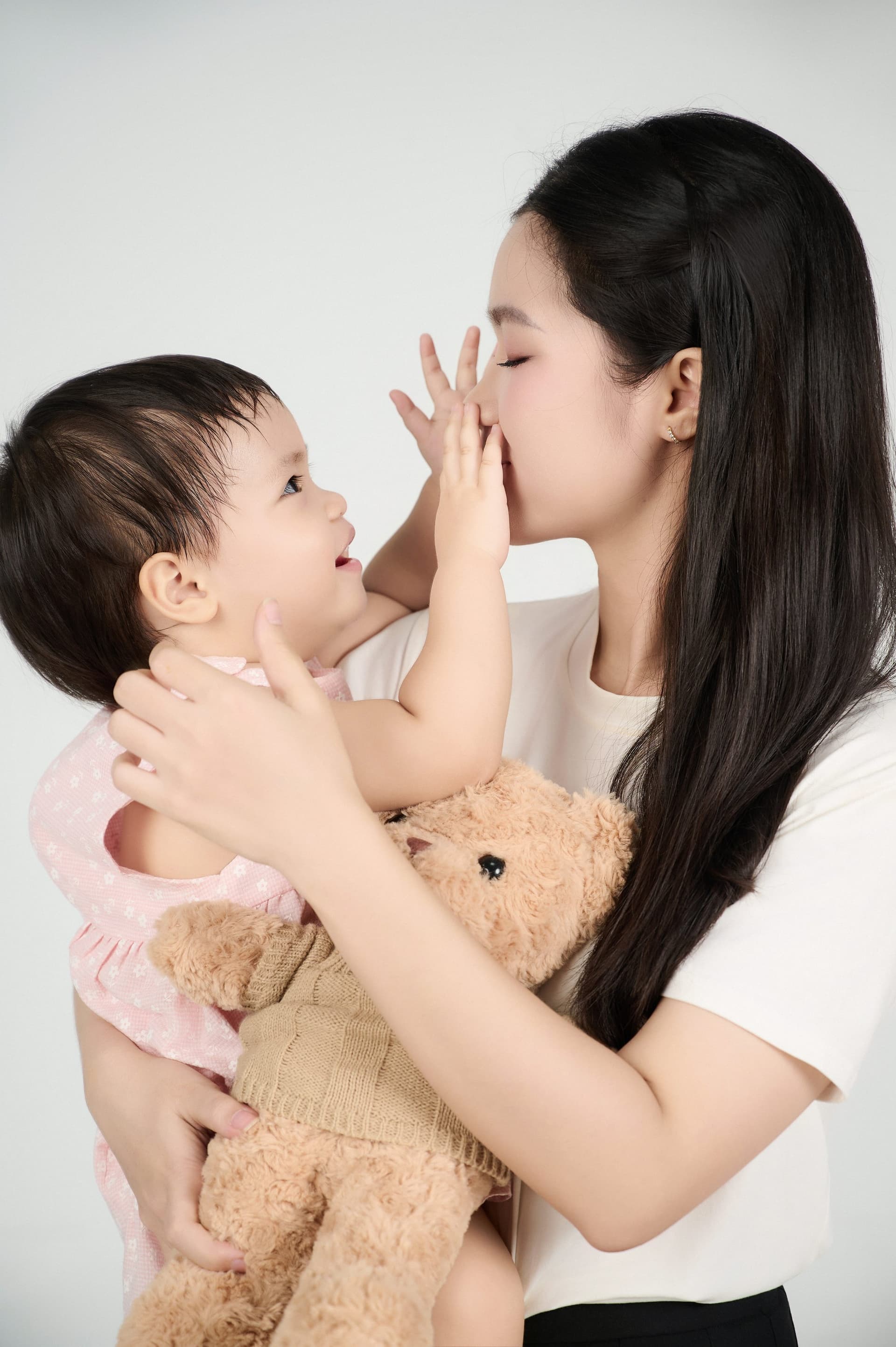 Bé lớn đứng tựa đầu, ngước mắt nhìn mẹ đang bế em bé ngủ trên vai dịu dàng