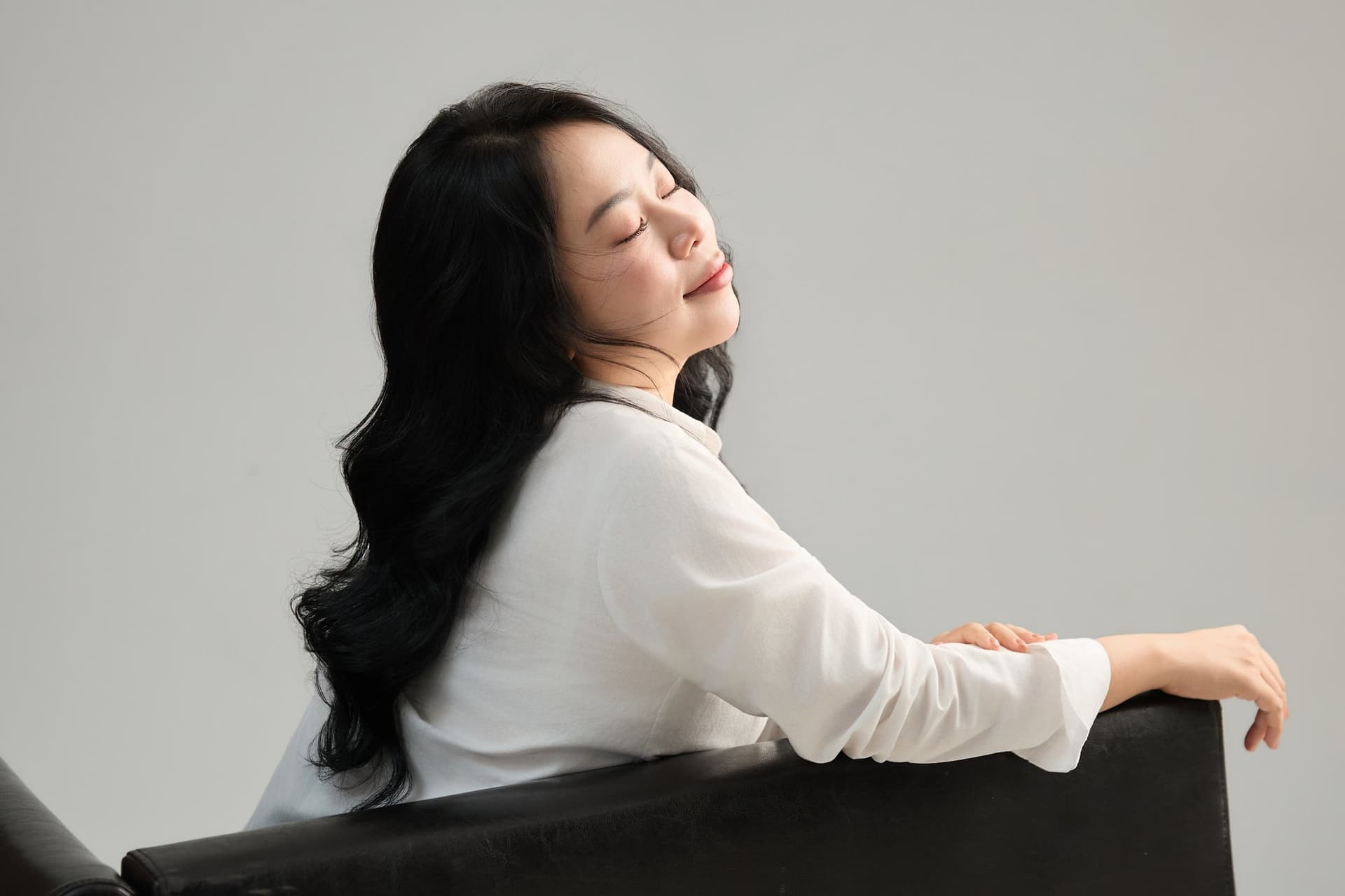 Cô gái áo trắng ngồi tựa cánh tay lên bàn, vẻ thanh thoát giữa ánh sáng dịu — một niềm vui nhẹ nhàng