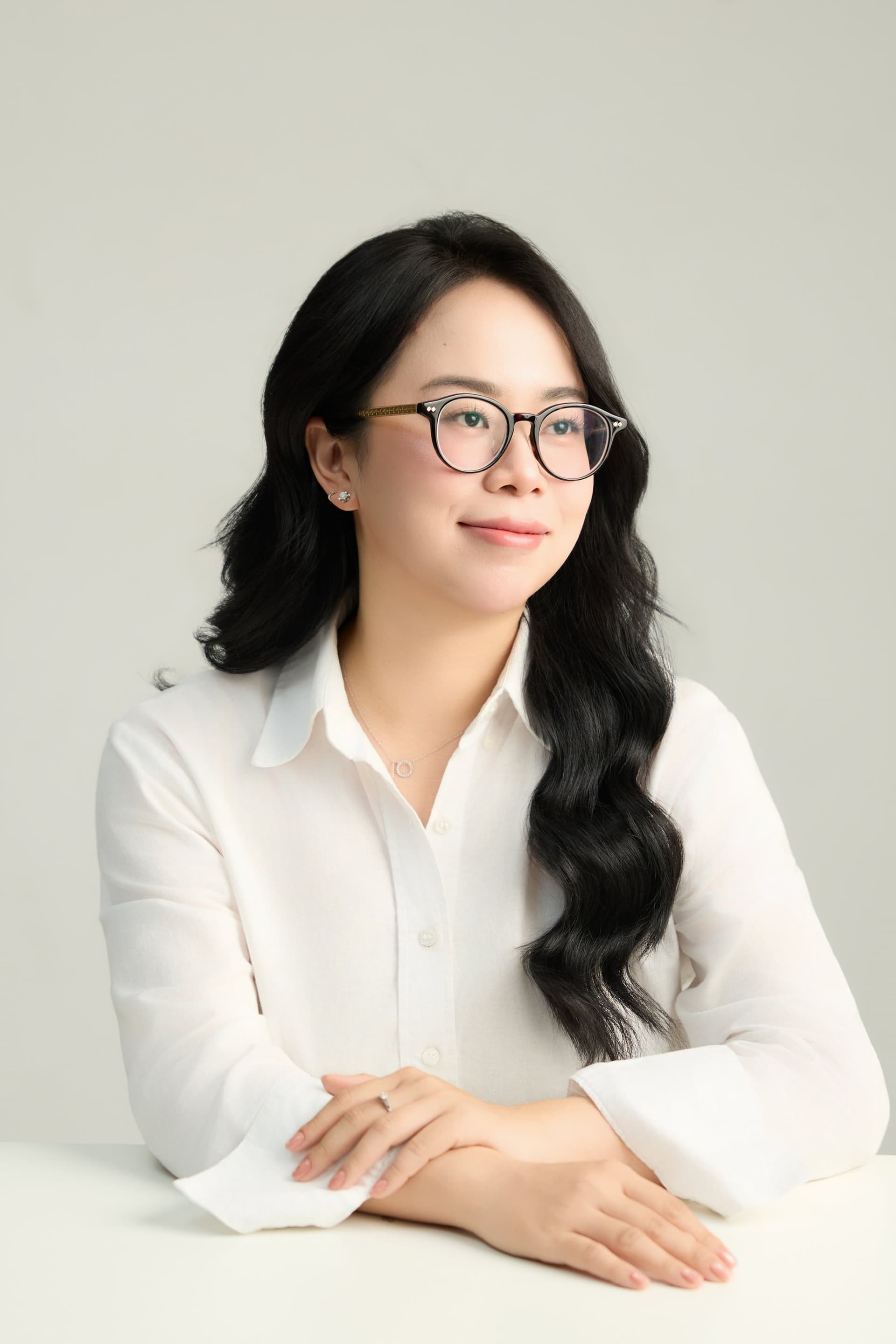 Cô gái đeo kính, ngồi tựa cằm lên bàn tay, vẻ trầm tư — người phụ nữ đứng giữa nhiều ngã ở tuổi ba mươi