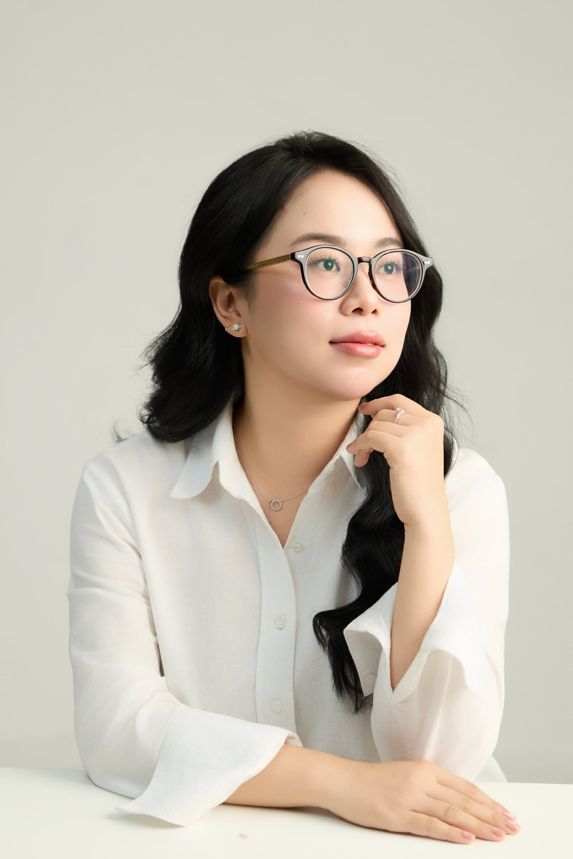 Cô gái đeo kính, tay khẽ vuốt tóc, mỉm cười nhẹ — niềm vui không ồn ào của một người phụ nữ ba mươi