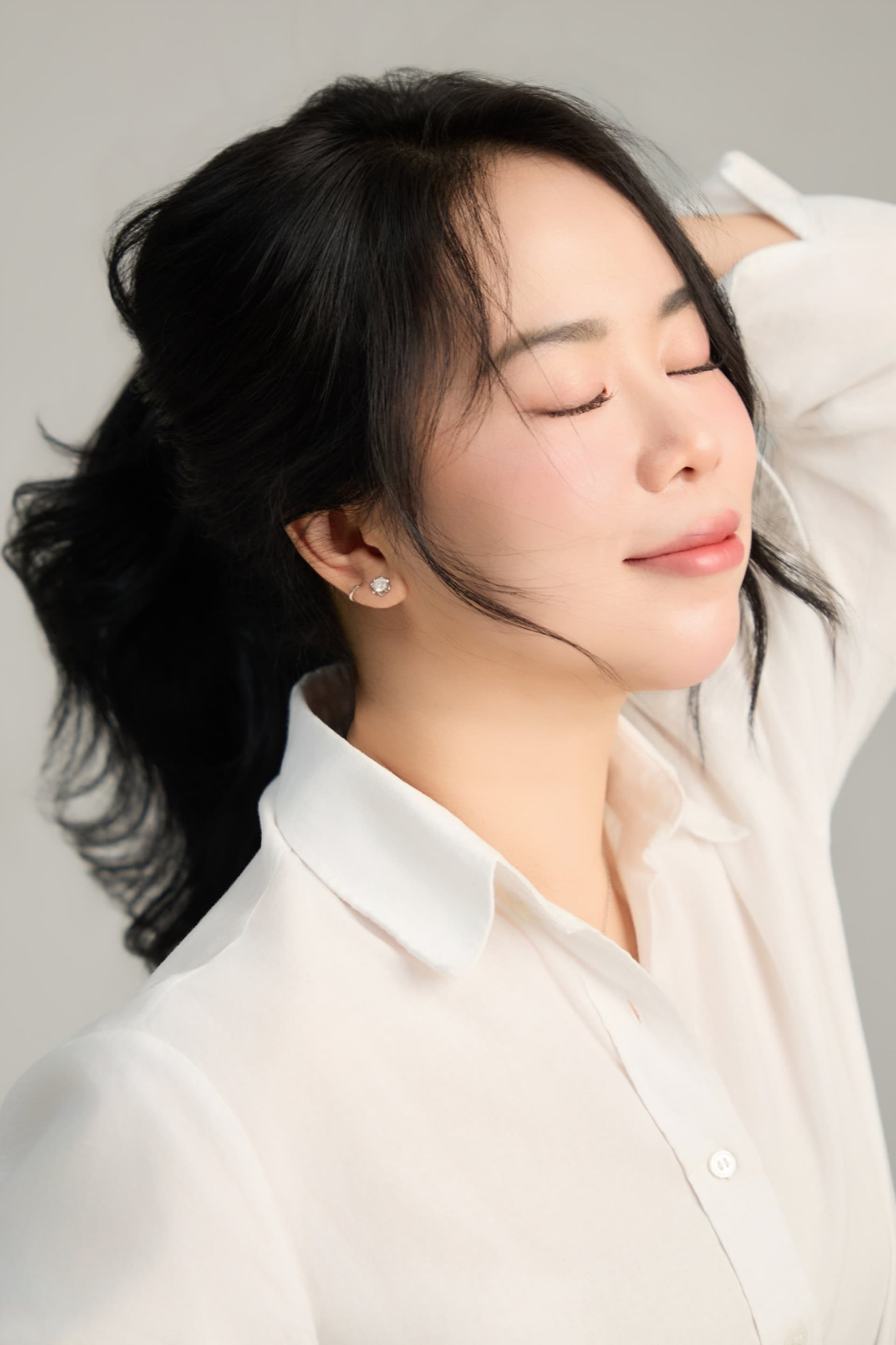 Cô gái khẽ vuốt tóc, mắt nhắm dịu, ánh sáng buông trên gương mặt — thấy vui, thấy nhẹ