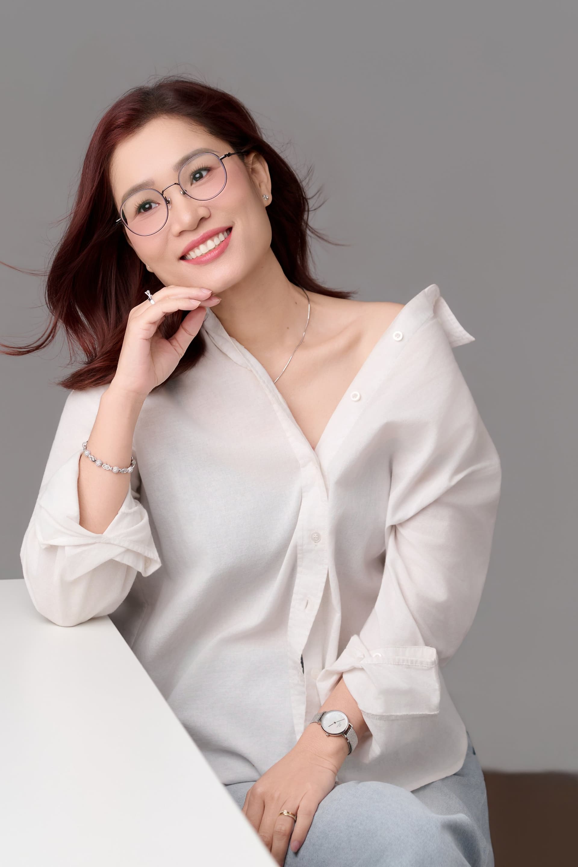 Chị Thể Nguyễn đeo kính, tựa cằm suy nghĩ nhẹ nhàng đầy vẻ thông thái ấm áp, nét mặt an nhiên tự tại