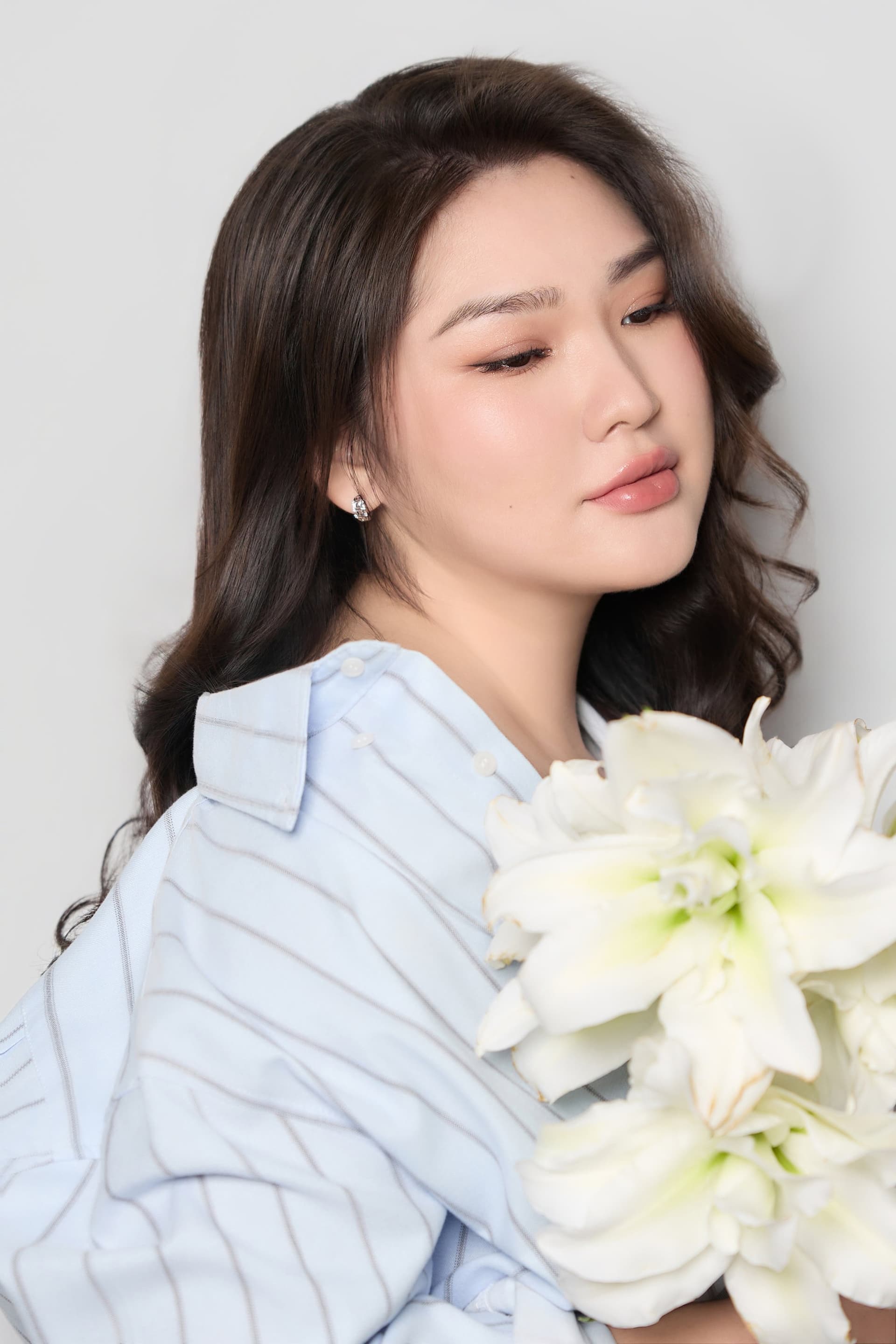 Trâm Huỳnh mỉm cười rạng rỡ và ôm bó hoa ly trắng tinh khiết bên khung cửa