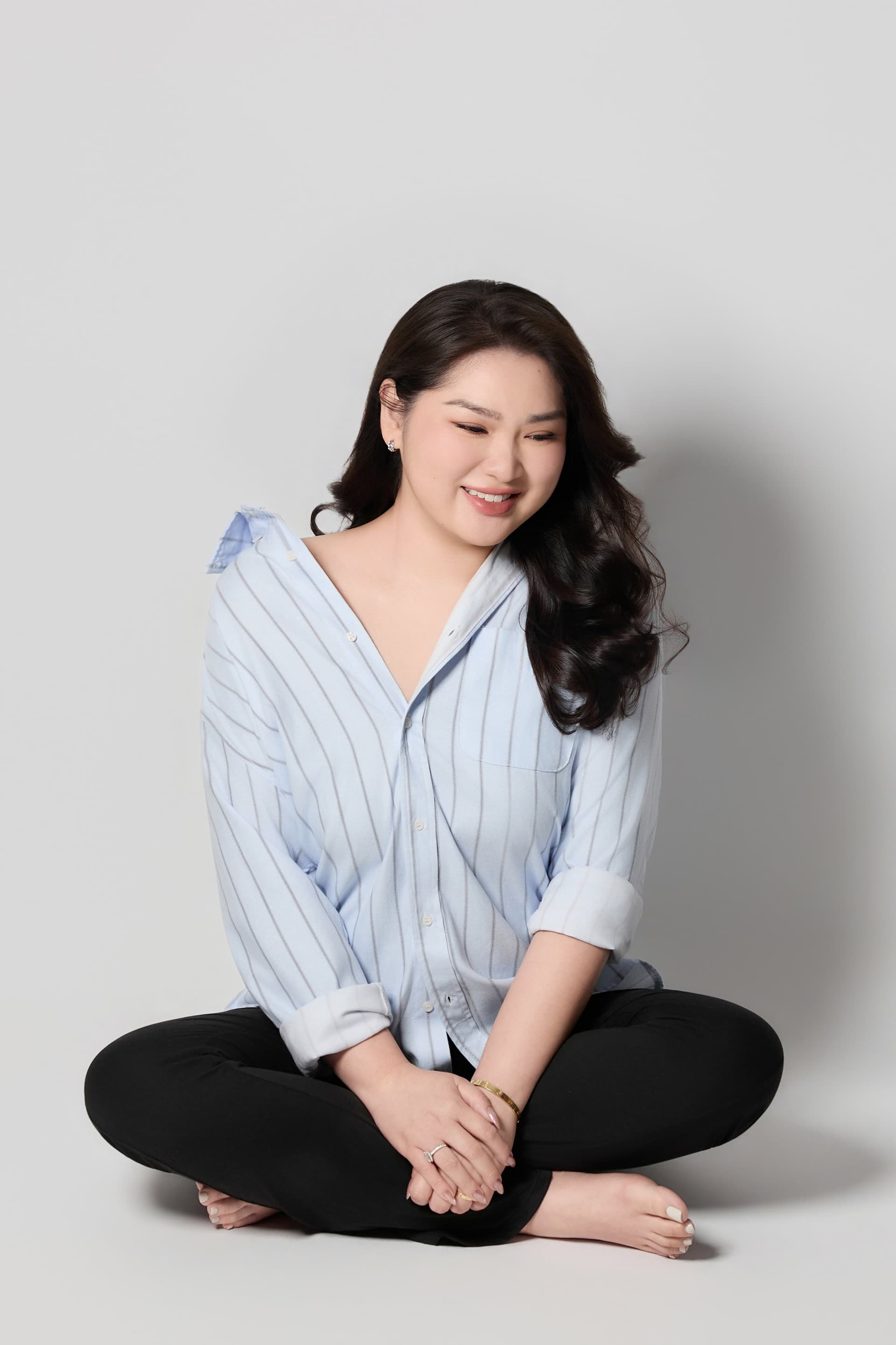 Trâm Huỳnh ngồi xếp bằng trên sàn gỗ mỉm cười hạnh phúc đầy viên mãn