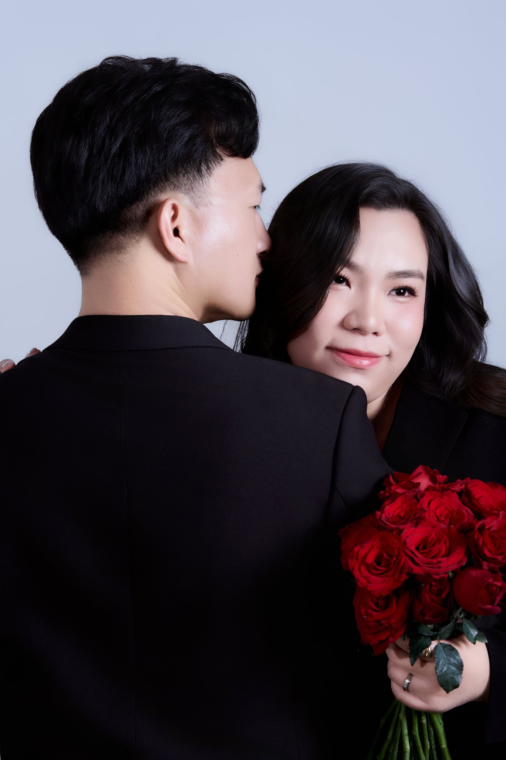 Người chồng khẽ tựa đầu thì thầm bên tai người vợ cùng bó hoa hồng đỏ thắm ngọt ngào